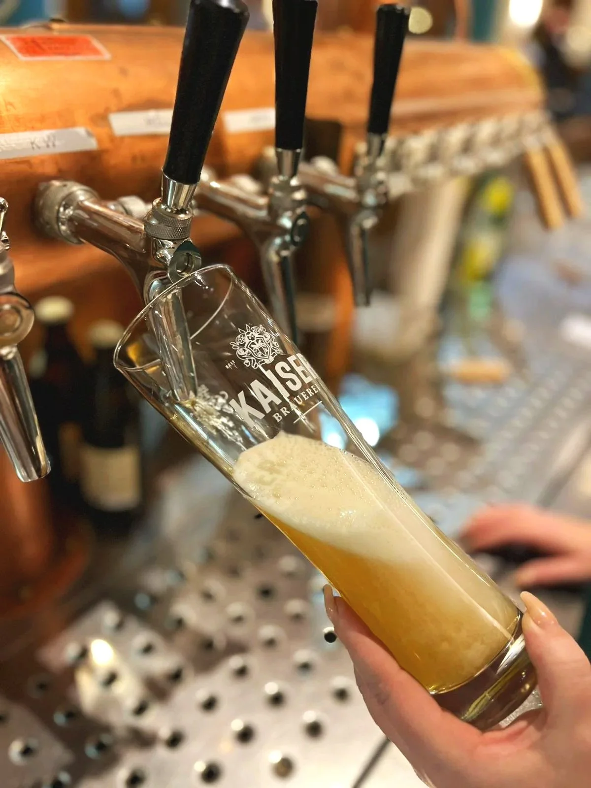  Ein Barman an der Theke bei der Arbeit, er zapft ein Bier, Name und Logo der Kaiser Brauerei sind zu erkennen. 