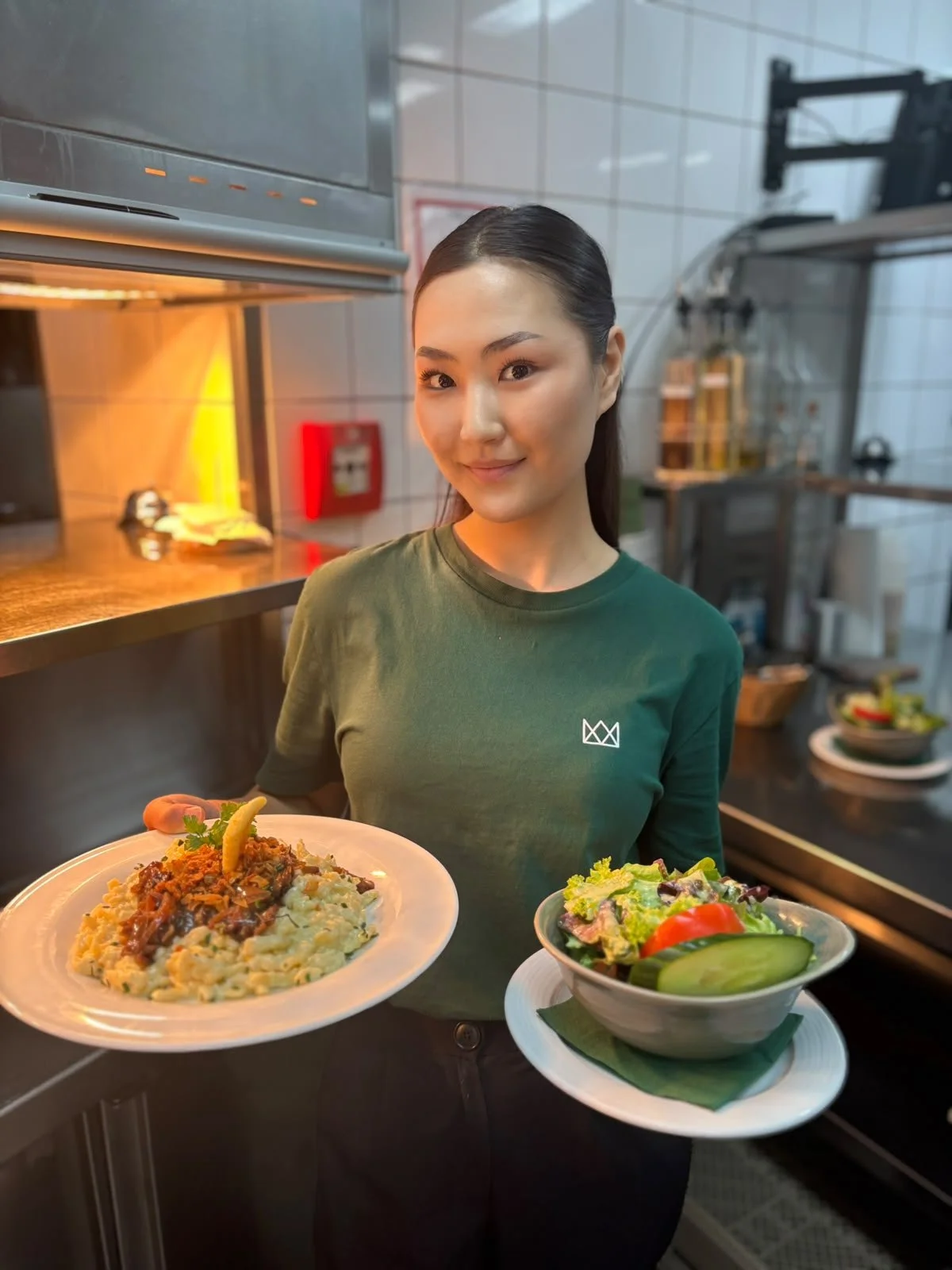  Eine Bedienung hat eine Bestellung in den Händen: einen Teller Käsespätzle und einen gemischten Salat, auf ihrem T-Shirt sind Name und Logo der Neuen Krone zu erkennen. 
