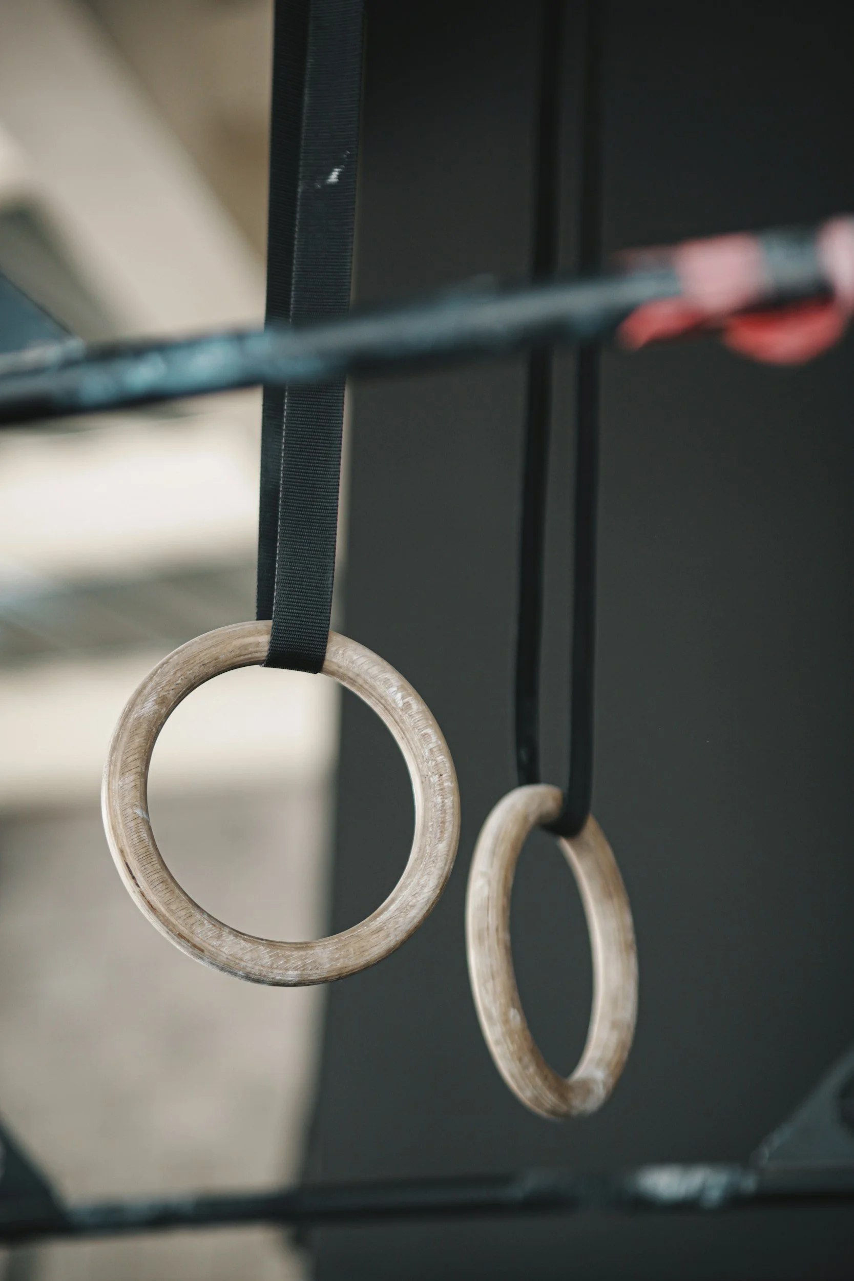 Two wooden gymnastic rings hanging from black straps attached to a black metal frame.