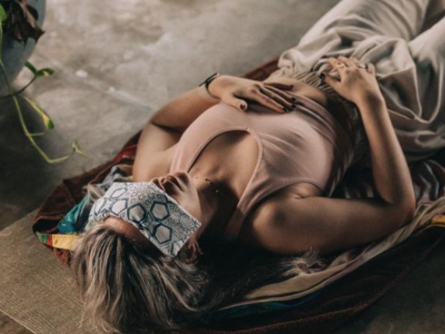A woman lying on a blanket with a sleep mask on, resting on her side with one hand on her stomach.