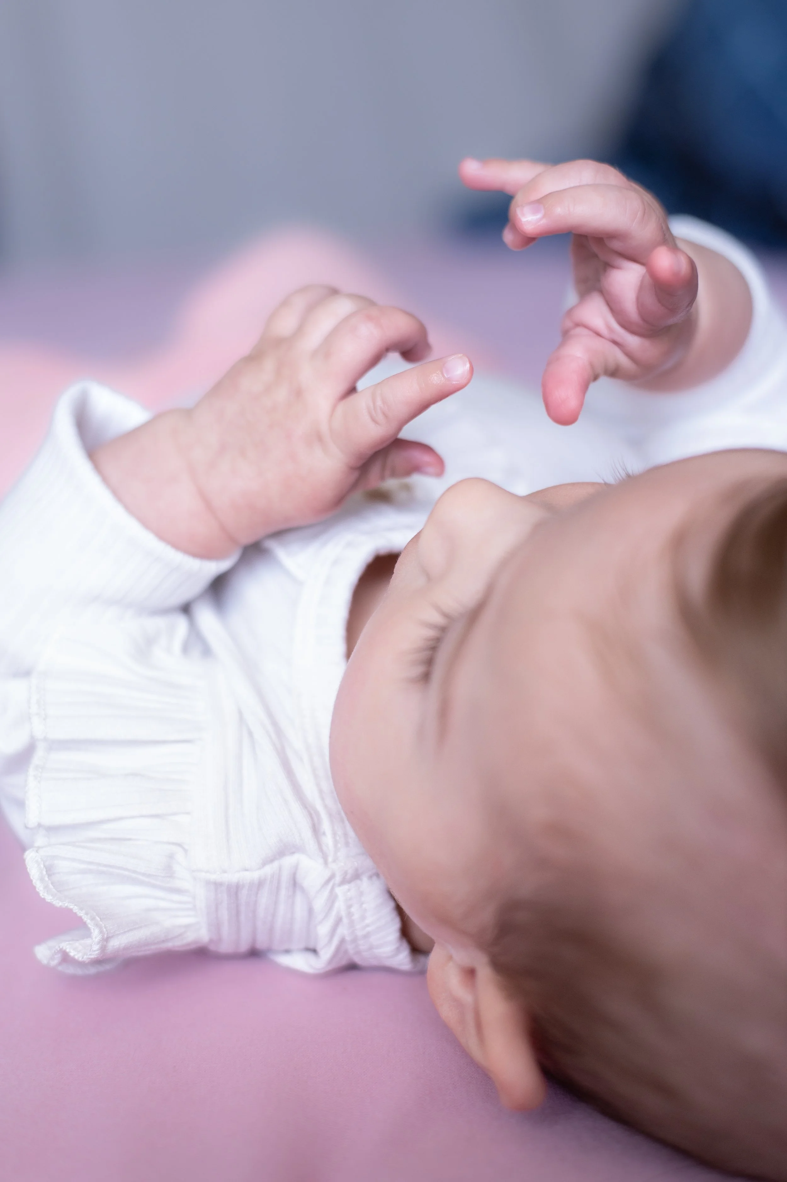 Bébé dormant allongé sur une surface rose, mains proches du visage, vêtue d'un vêtement blanc., photo enfant, photographe de famille, photographe de famille à saintes, photographe à saintes