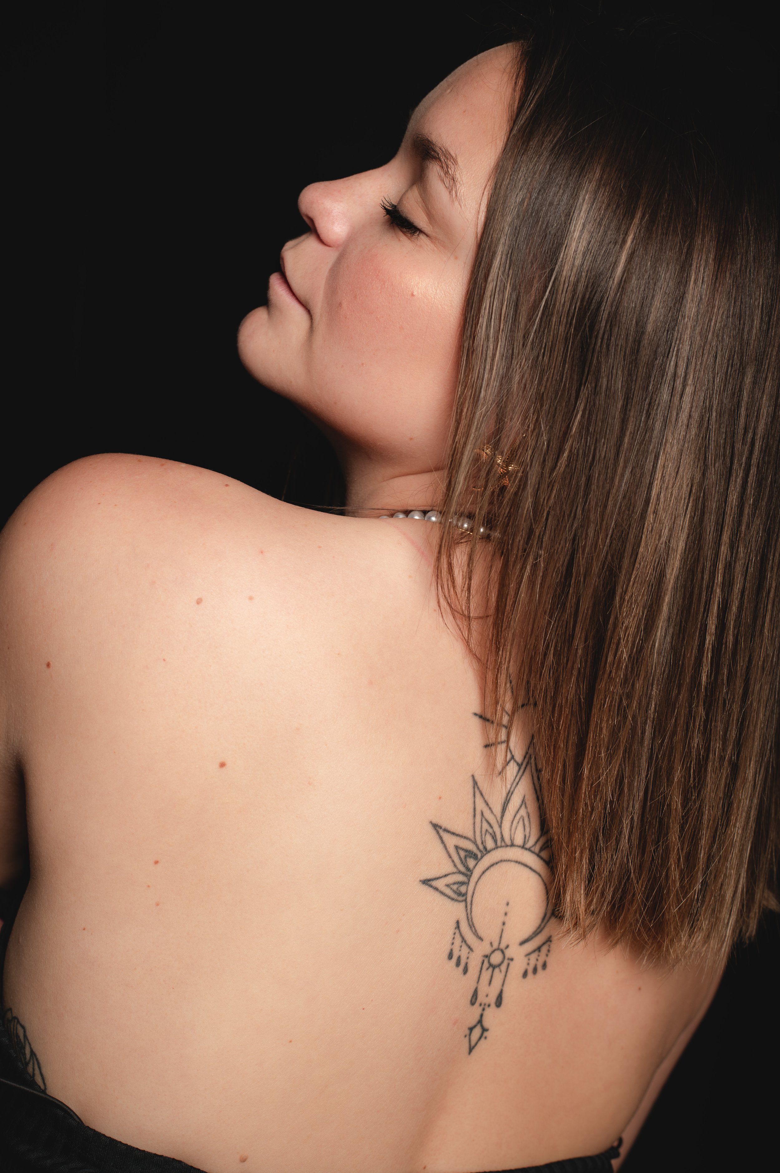 Profil de femme avec tatouage floral sur le côté gauche du torse, longs cheveux bruns, peau claire, regard vers le haut, fond noir, Saujon, royan, saintes, Charente maritime, photographe Charente maritime