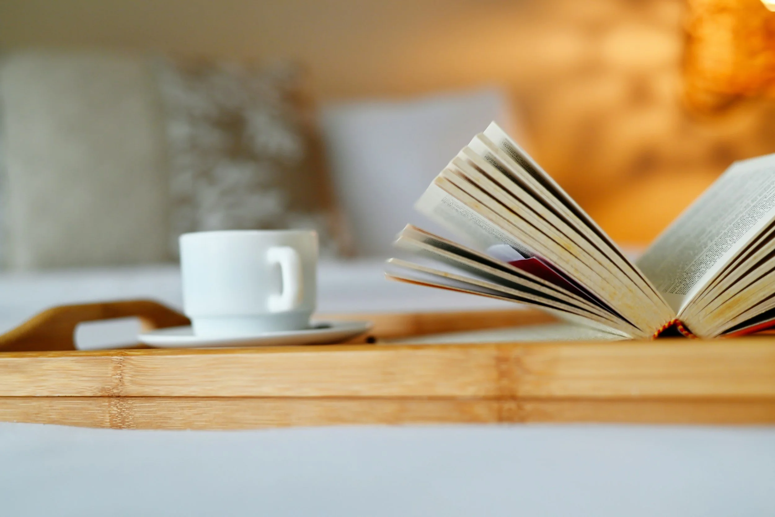 Open book next to a white coffee cup on a wooden tray.