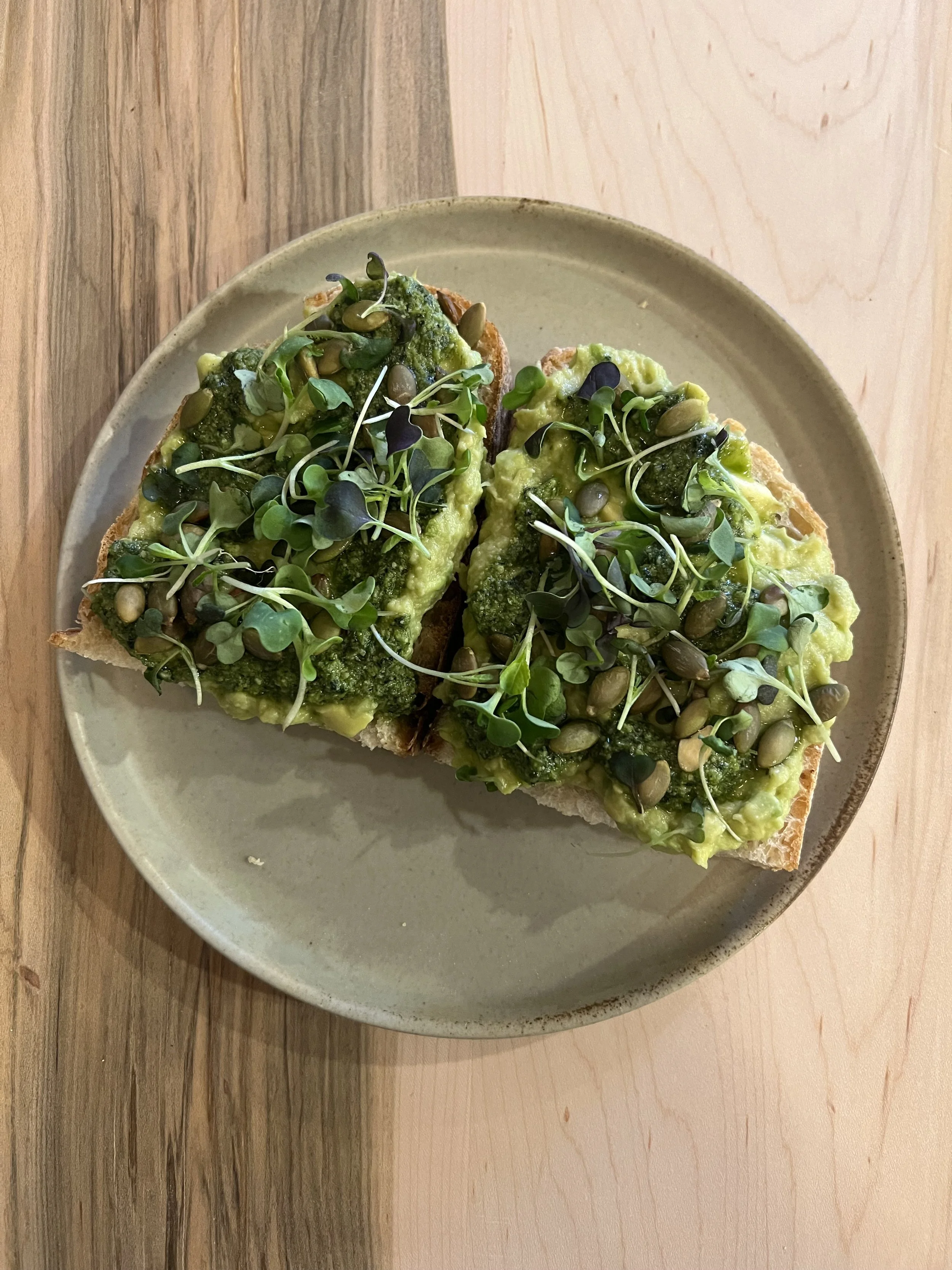 Toast topped with avocado, green sauce, and microgreens on a beige plate.
