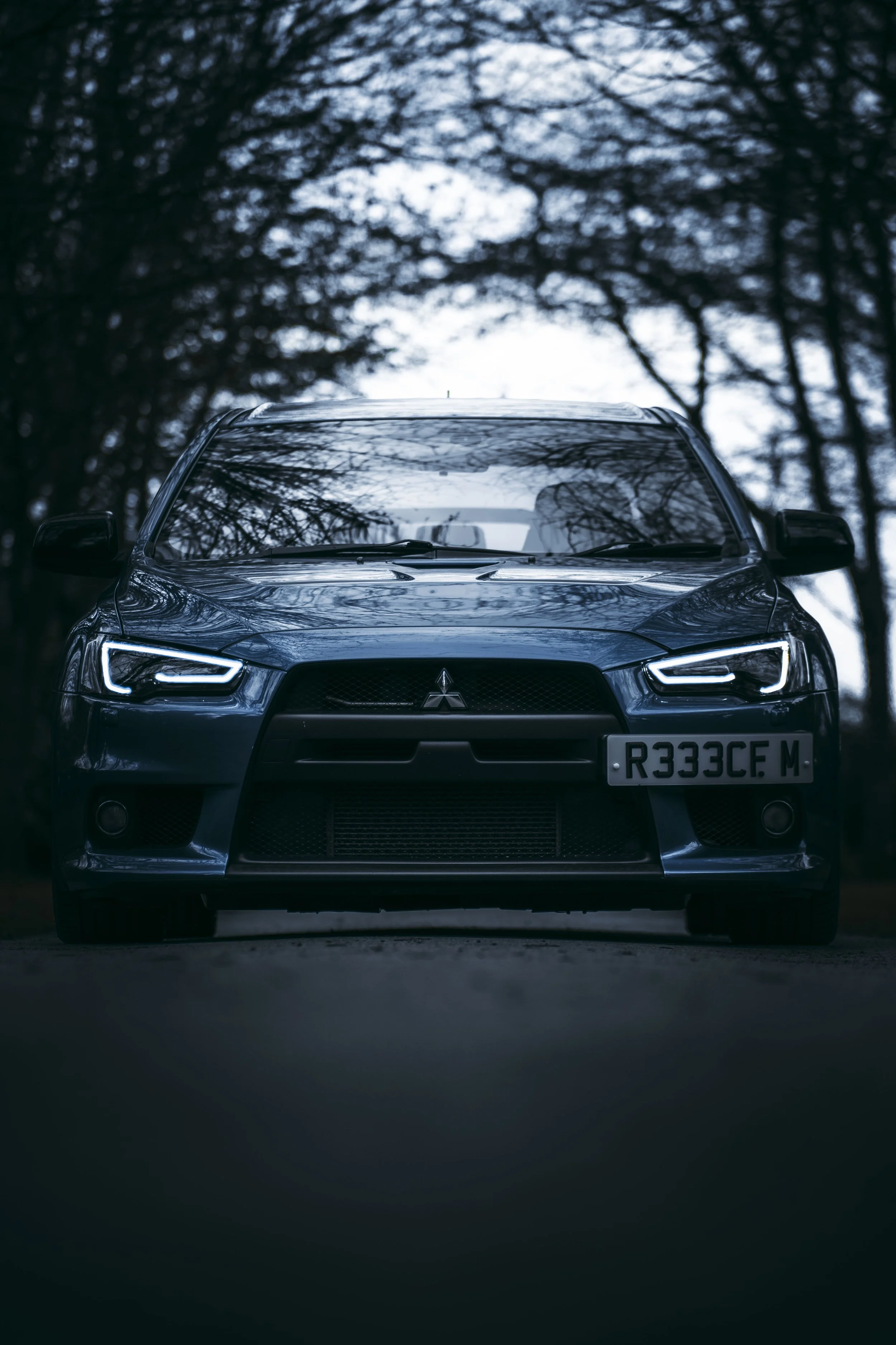 Front view of a dark blue Mitsubishi car parked outdoors with trees in the background.
