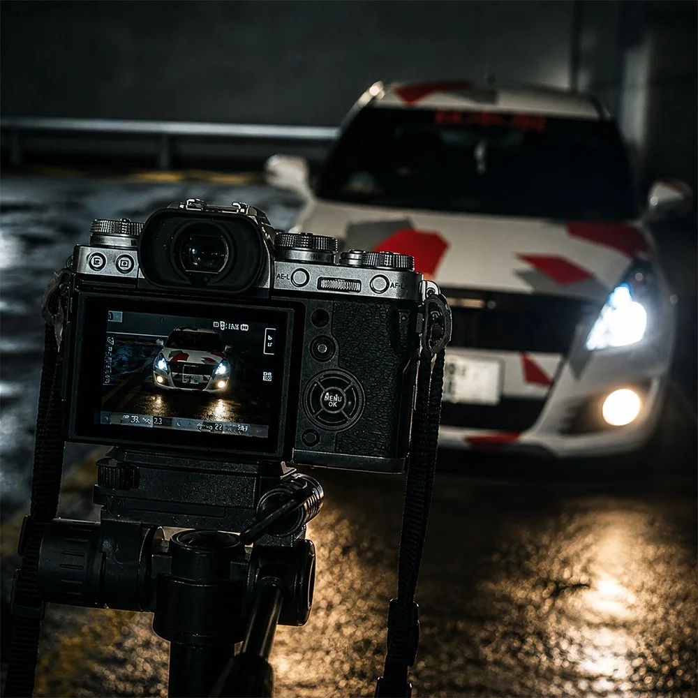 Camera capturing a car with a racing stripe design on a wet, illuminated road at night.