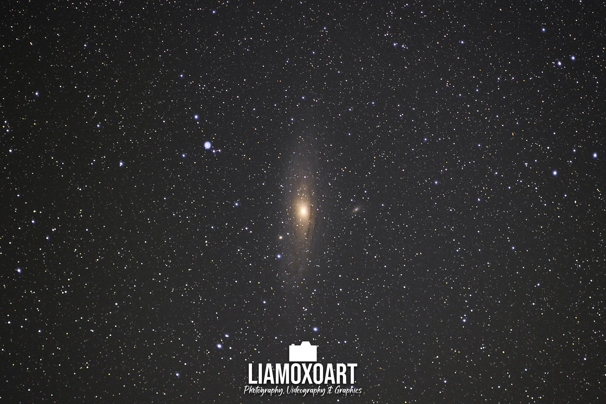A wide view of the night sky filled with countless stars and a faint galaxy visible near the center.