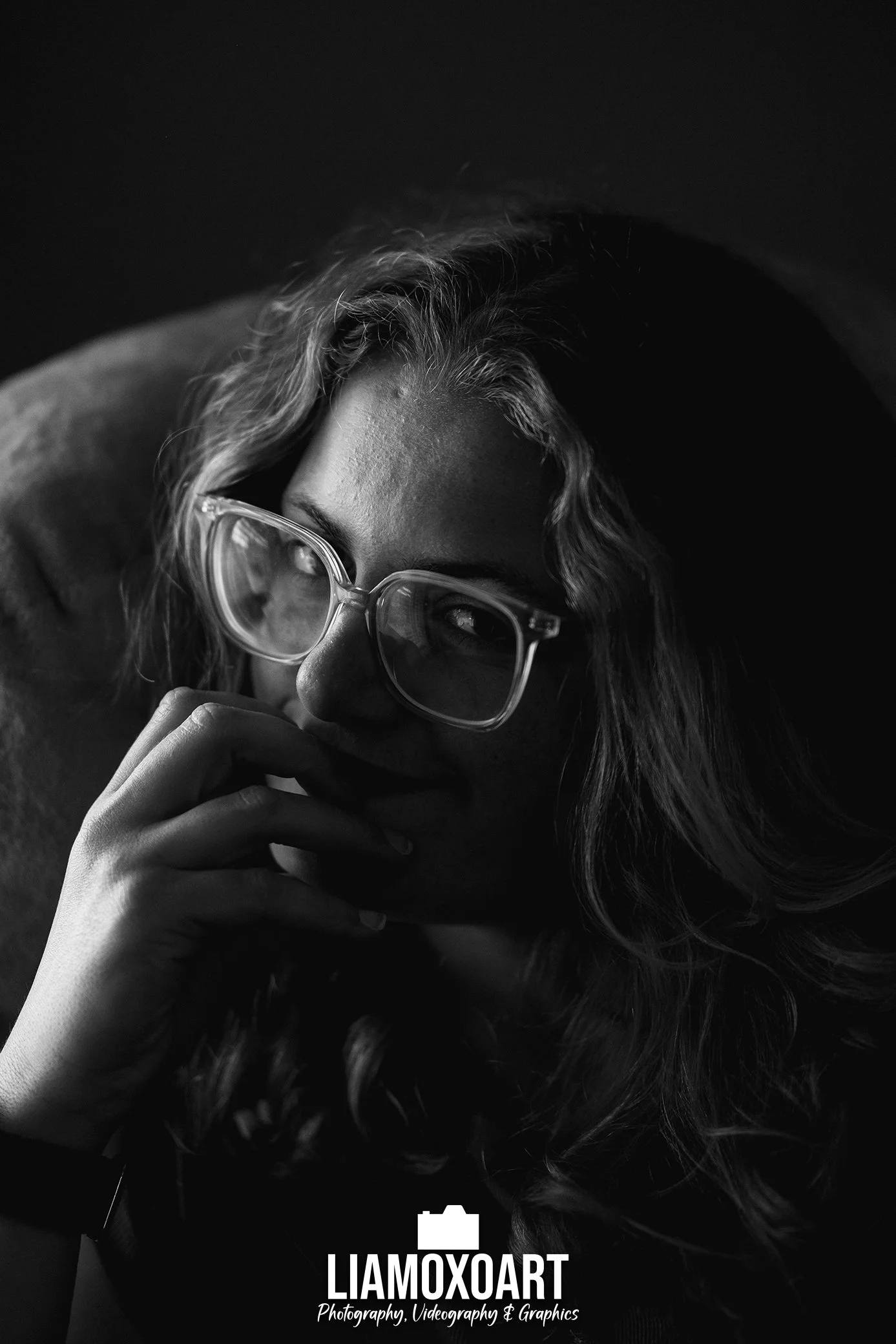 Black and white close-up portrait of a woman with glasses, curly hair, and a thoughtful expression.