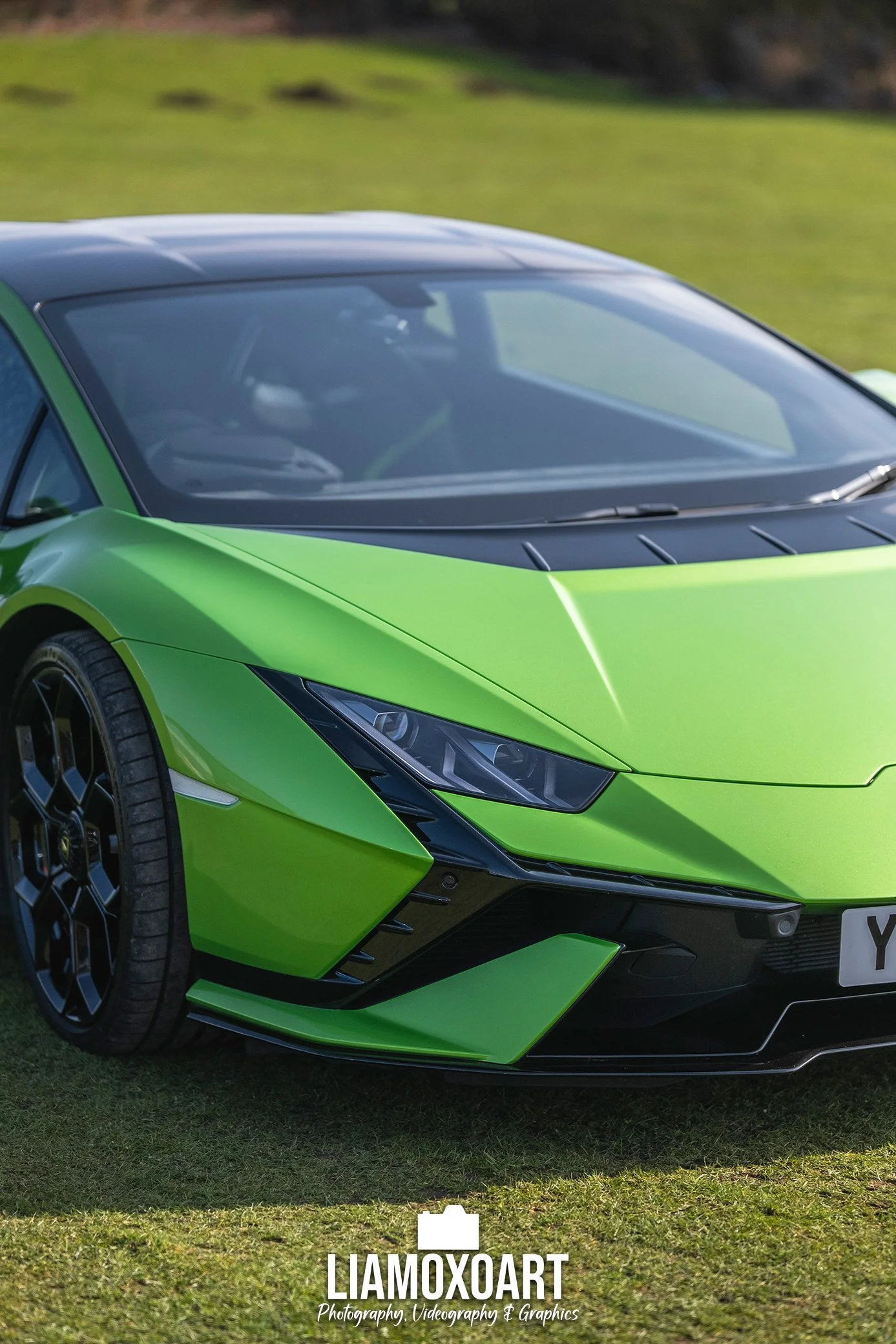Close-up of a lime green sports car with black accents parked on grass, featuring sharp angular design and sleek headlight design.