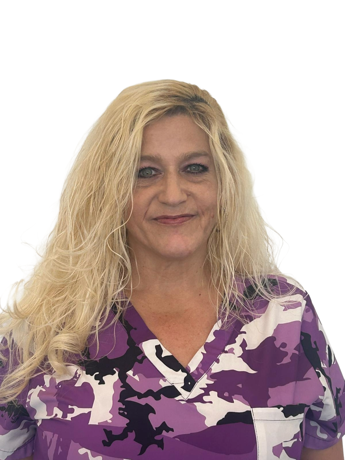 A woman in purple scrubs with Halloween-themed prints standing in front of a glass door with a black letter logo, pointing at the logo and smiling.