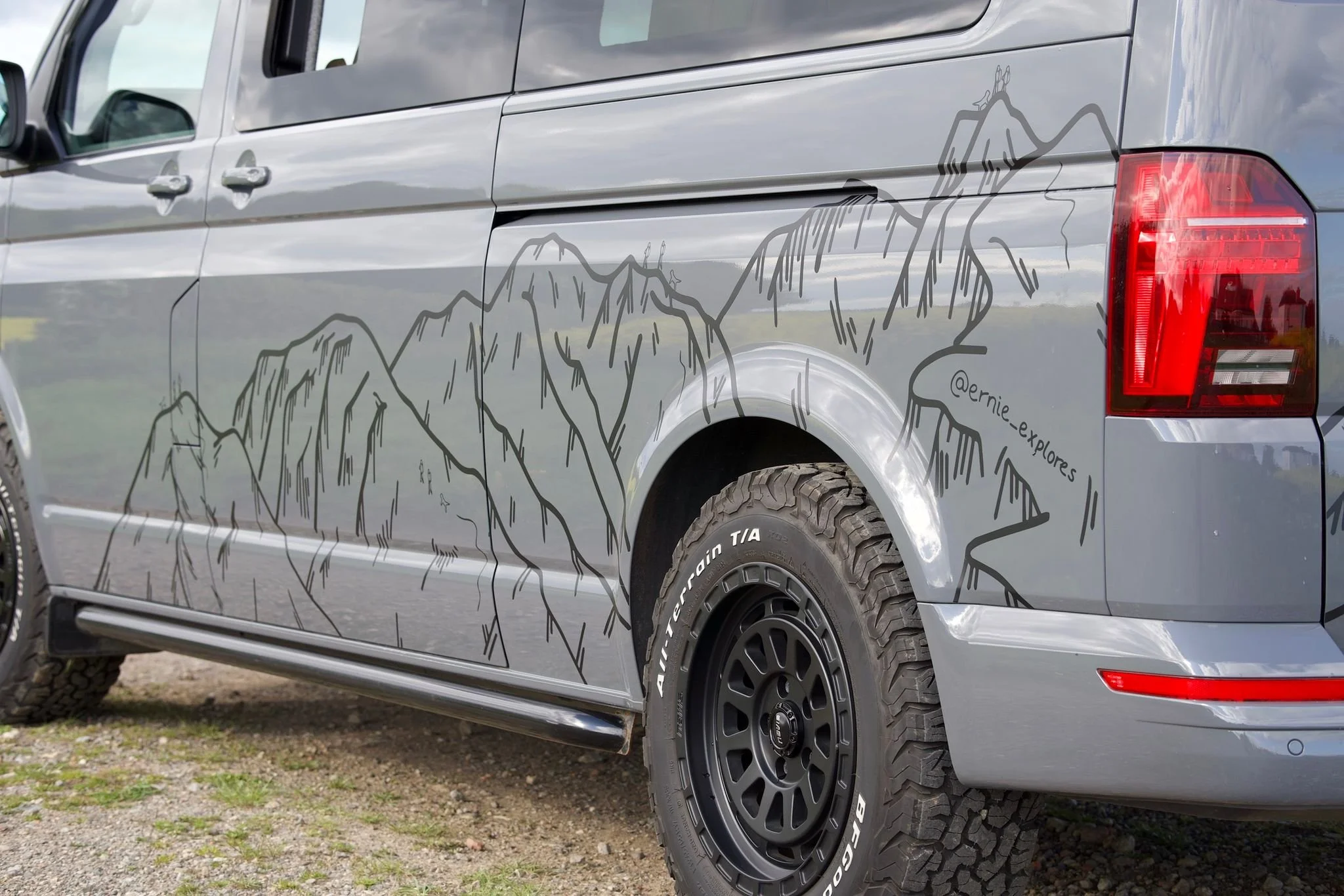 Two white vans with mountain landscape decals, parked on a dark gray surface.