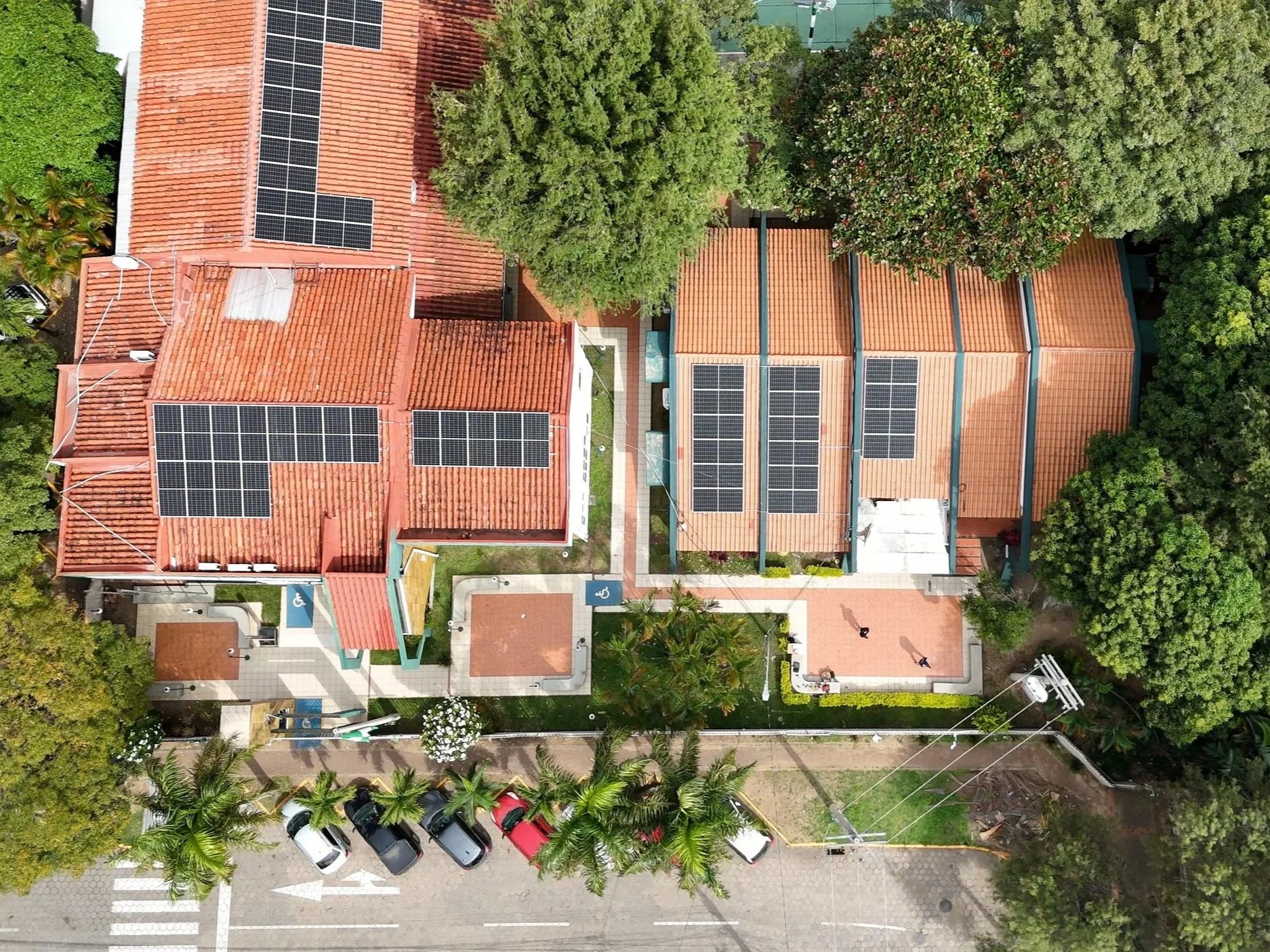 Vista aérea de un conjunto de edificios residenciales con techos rojos y paneles solares, rodeados de árboles y vehículos estacionados en la calle. Santa Cruz de la Sierra Bolivia