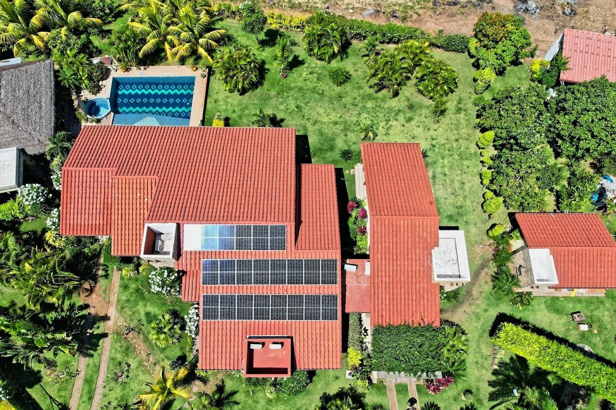 Vista aérea de una casa con tejados de teja roja, un patio con césped, árboles y plantas, y una piscina en la esquina superior izquierda.