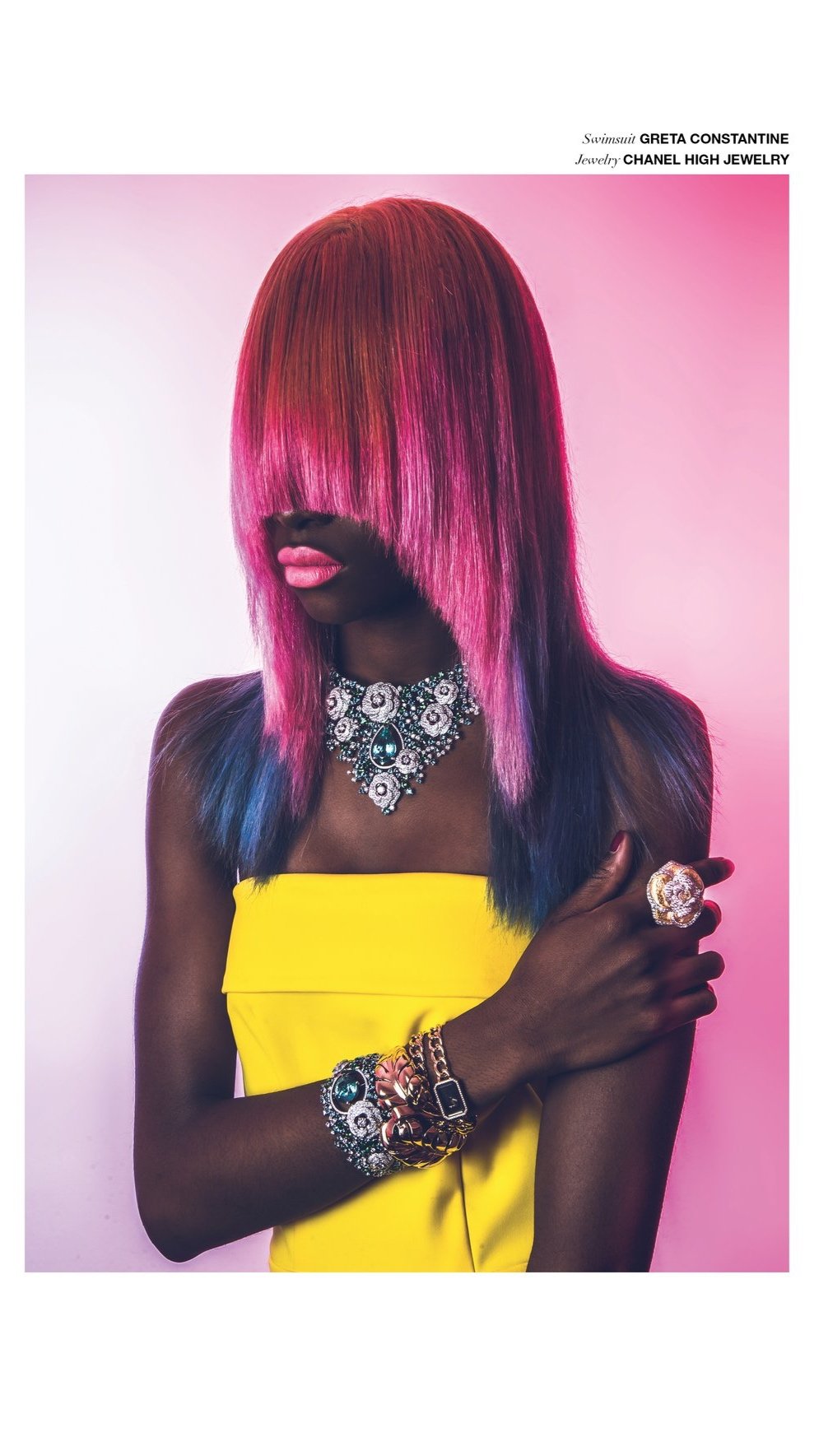Une femme portant des bijoux orne des boucles d'oreilles, un collier, un bracelet et une bague, avec un maquillage rose, des cheveux colorés en dégradé de rose, violet et bleu, et une robe jaune
