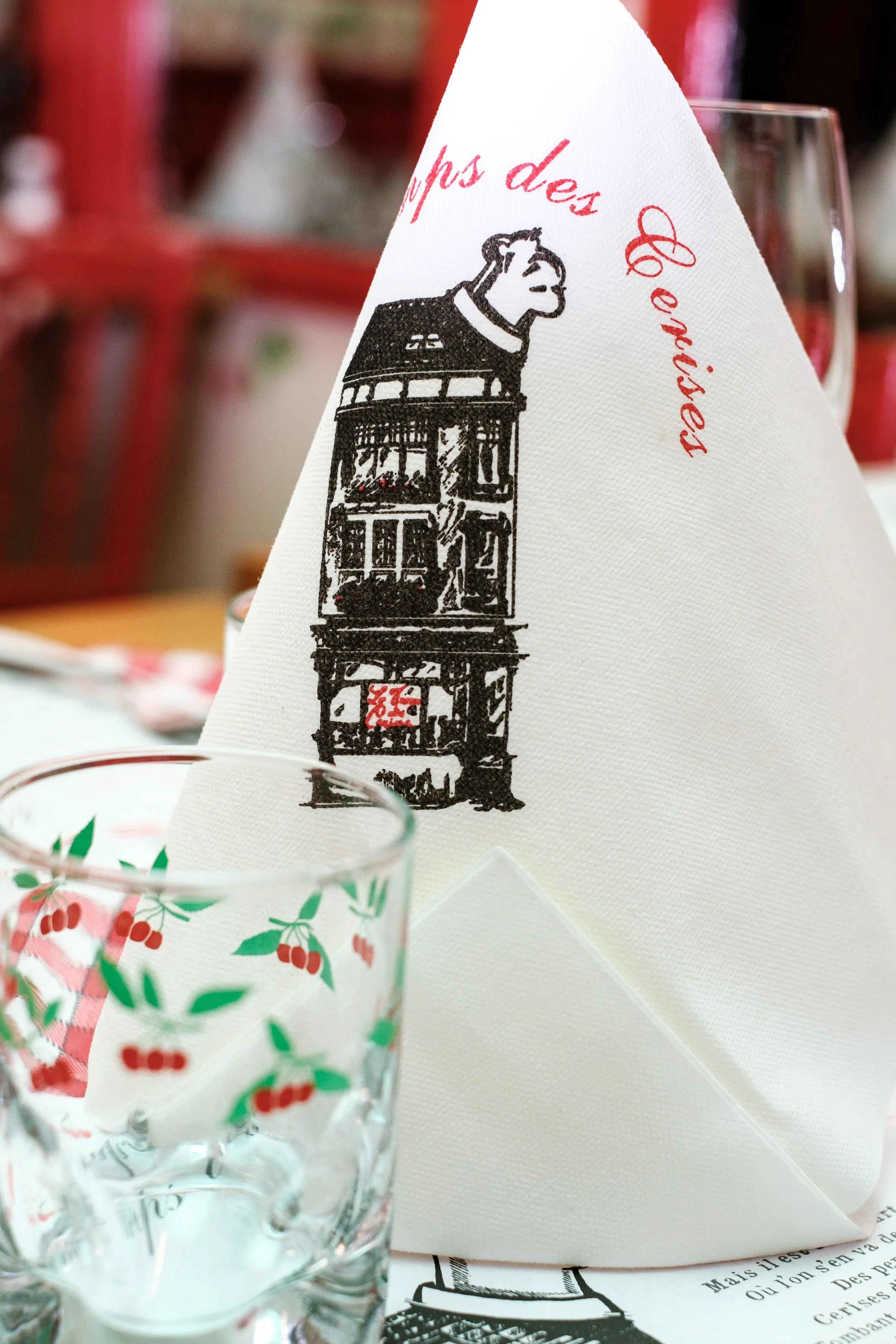 Une nappe blanche avec une illustration d'un bâtiment en noir et une tête de chien de race non identifiée sur le dessus. Il y a aussi un verre à moitié rempli devant.
