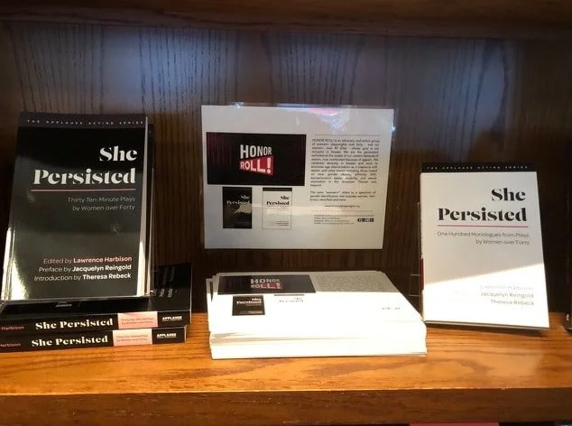 Books and pamphlets titled "She Persisted," displayed on a wooden shelf.