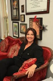 Woman sitting on a red velvet sofa in a room decorated with picture frames and holiday decorations.