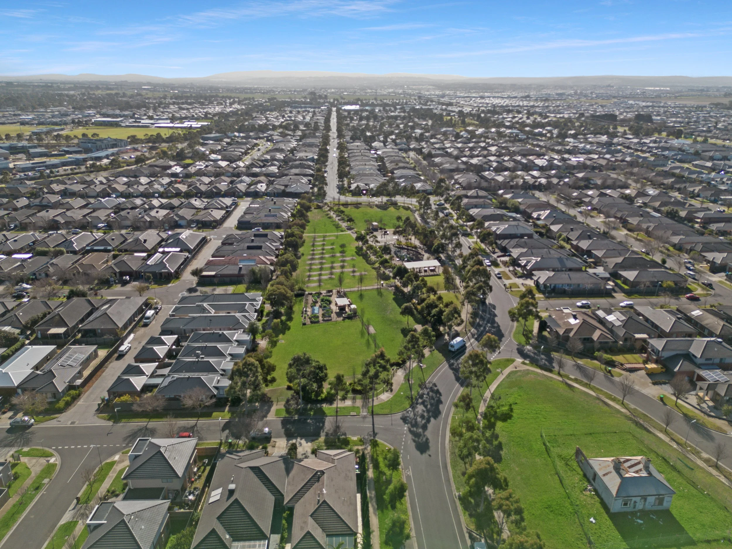 Aerial view of a suburban neighborhood with neatly arranged houses, a large park with trees and open grassy areas, and roads winding through the area.
