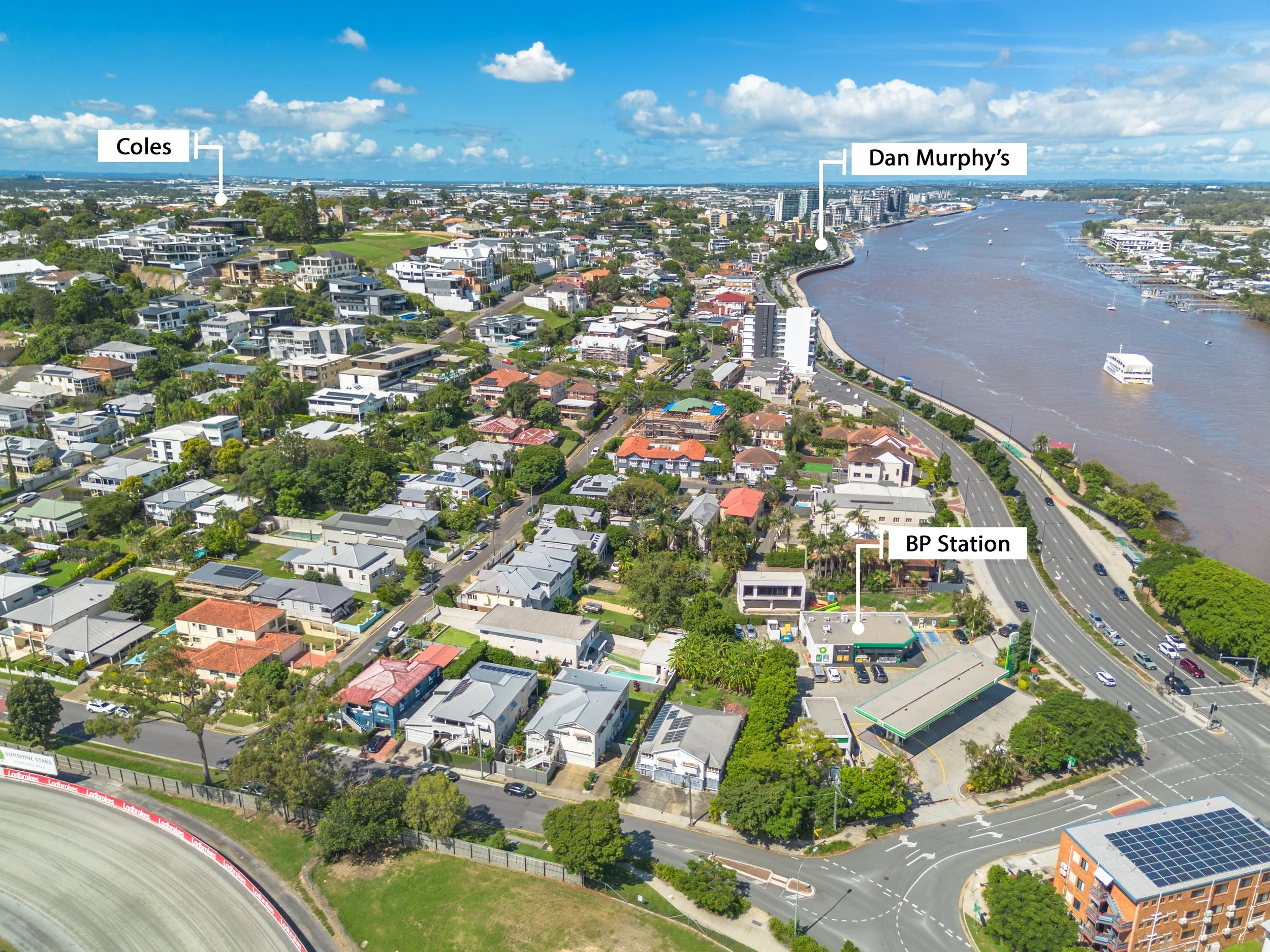 Aerial view of a neighborhood near a river with a BP station, houses, high-rise buildings, and labeled locations of Coles, Dan Murphy's, and BP station.