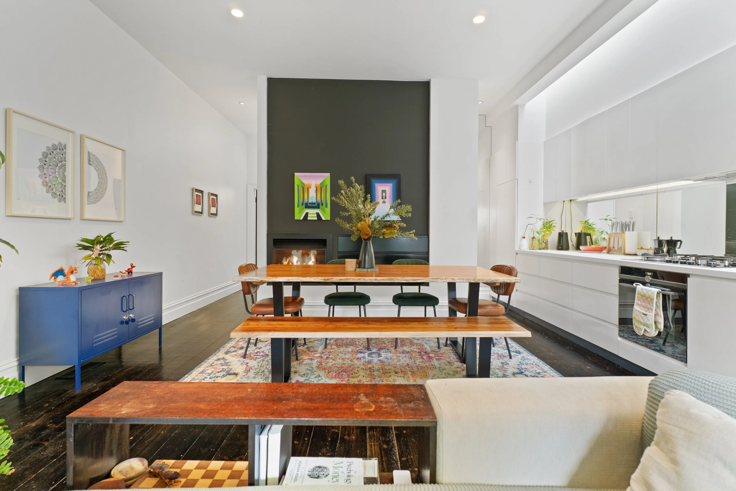 Modern open-concept living and dining area with a kitchen, featuring a dining table, fireplace, wall art, and decorative items.