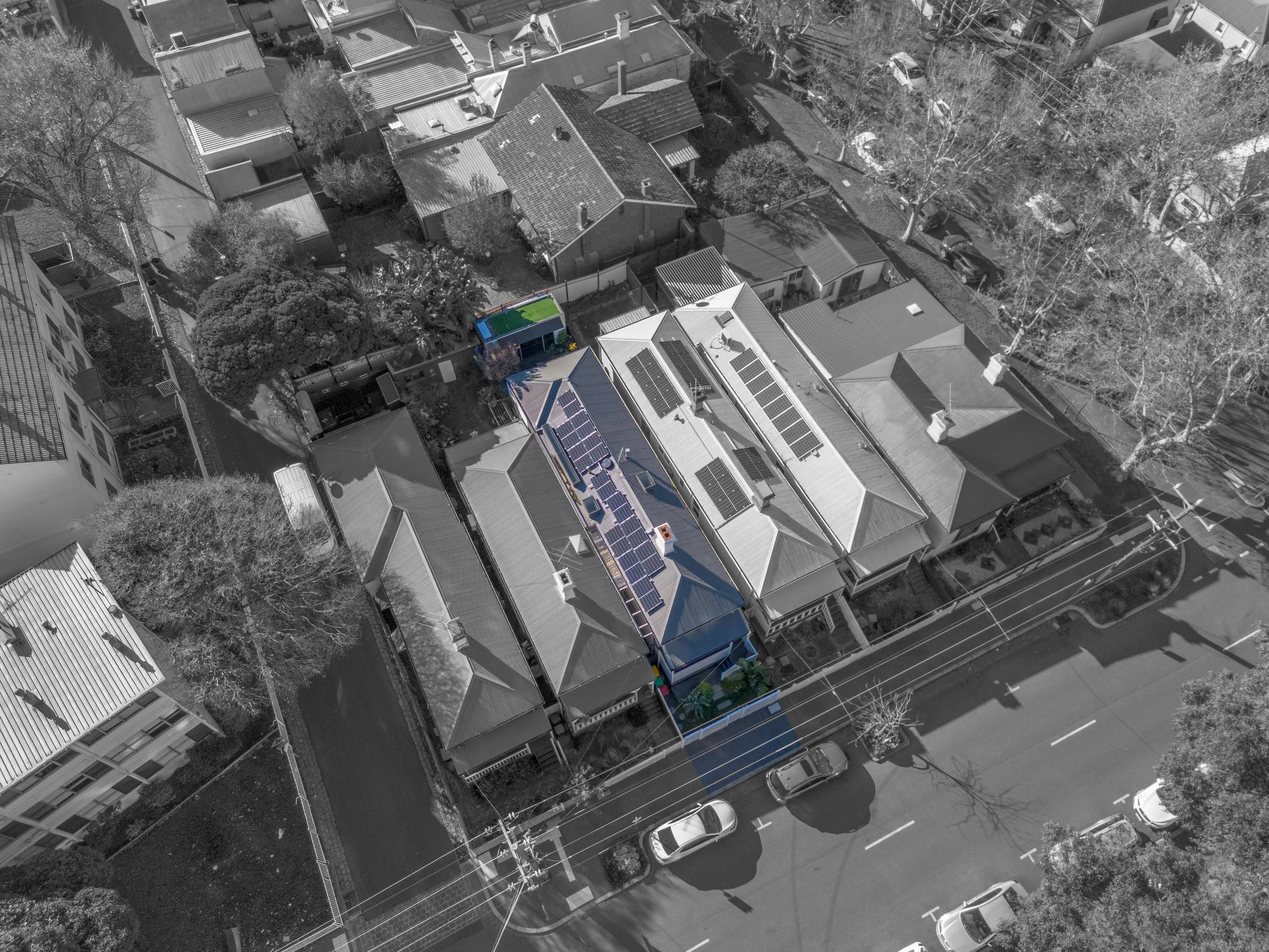 Aerial view of a neighborhood with a mix of houses and buildings, including a house with a swimming pool in the backyard surrounded by trees and greenery.