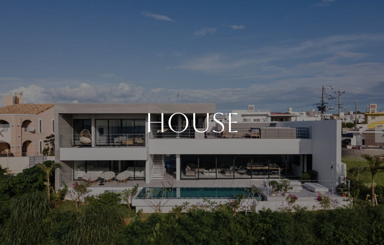 Modern white house with outdoor pool, patio, and lounge chairs in a lush green area under a partly cloudy sky.