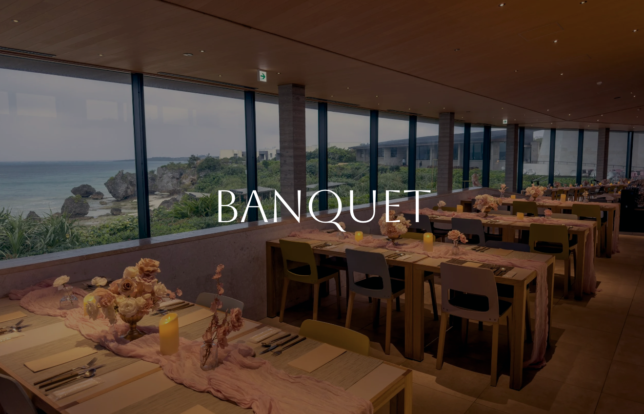 Elegant banquet dining area with long tables decorated with pink cloth runners, floral centerpieces, candles, and place settings, overlooking a scenic ocean view through large windows.