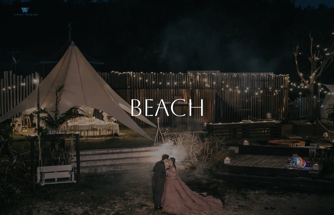 A romantic beach wedding scene at night with a couple dancing near the shore, illuminated by string lights, with a large white tent and decorated area for the event.