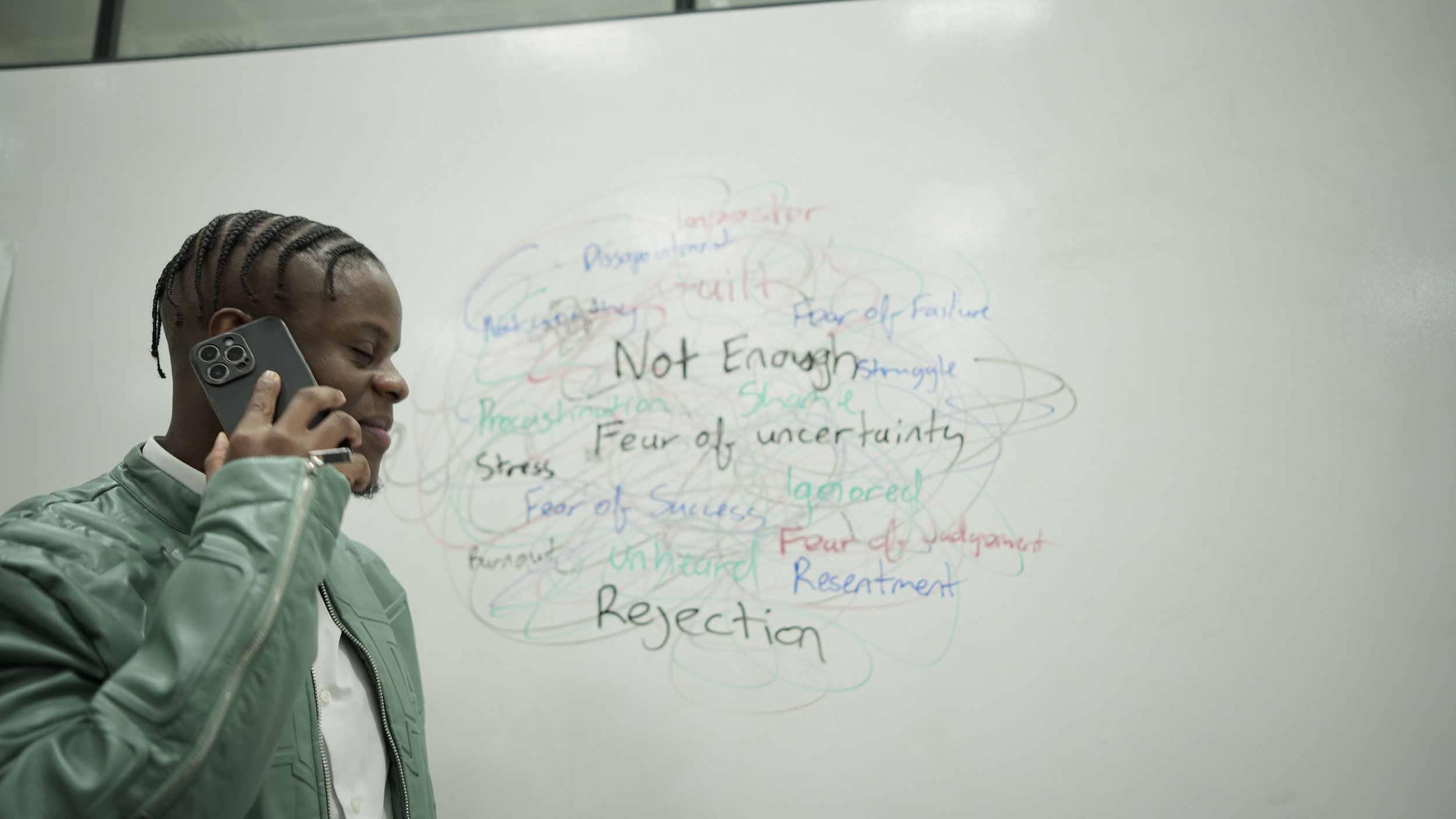 Person talking on a phone, standing near a whiteboard with words like 'Not Enough', 'Fear of Uncertainty', and 'Rejection' written on it in various colors.