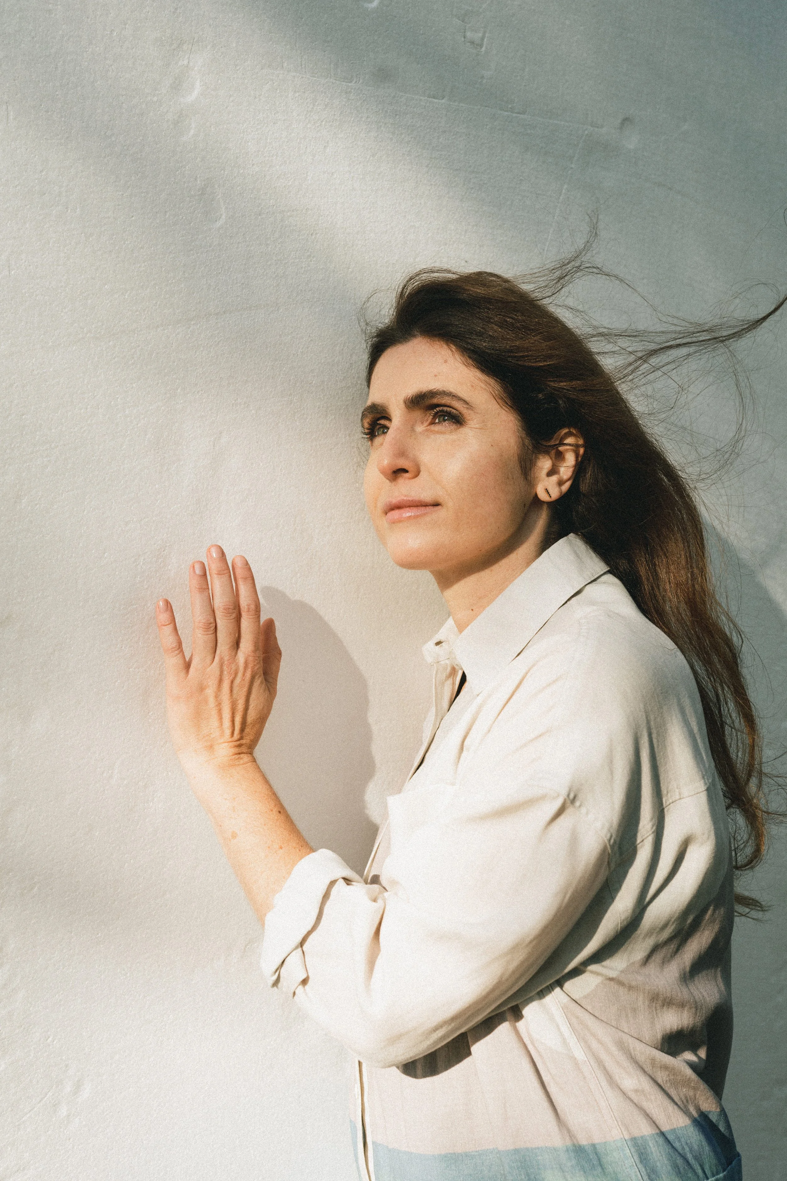 Frau lehnt an einer Wand, schaut nach oben, bei Sonnenlicht