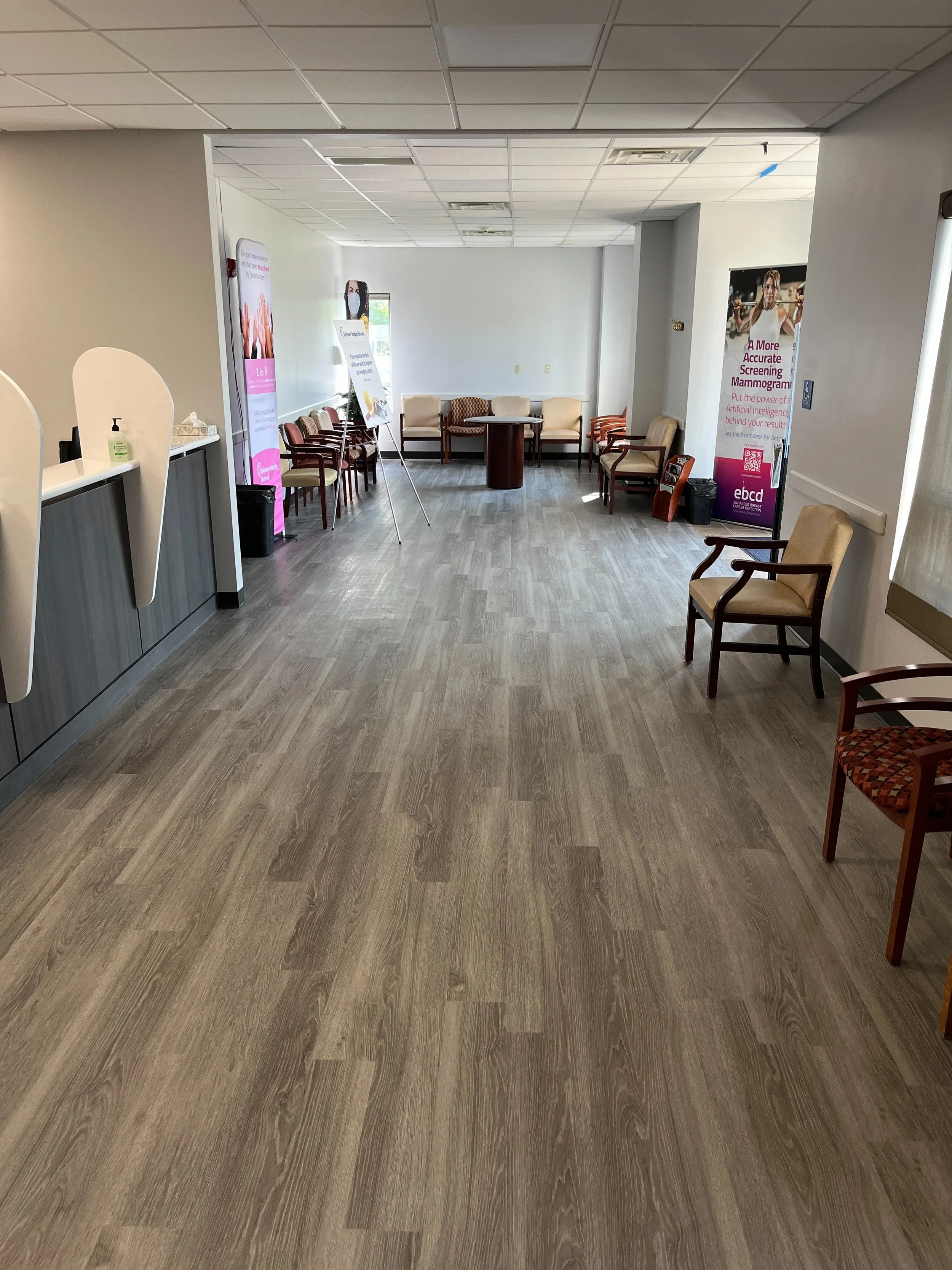 Empty waiting room with chairs along the walls, informational signs, and posters about mammograms and health screening.