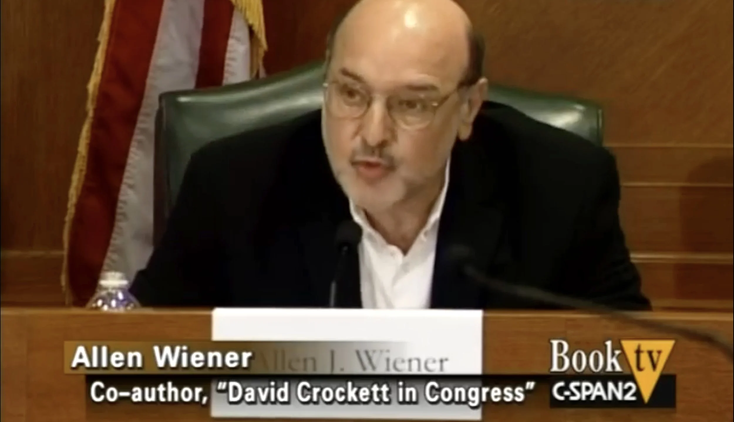 Allen Wiener sitting at a panel with a nameplate in front of him and a microphone, speaking during a C-SPAN2 Book TV event.
