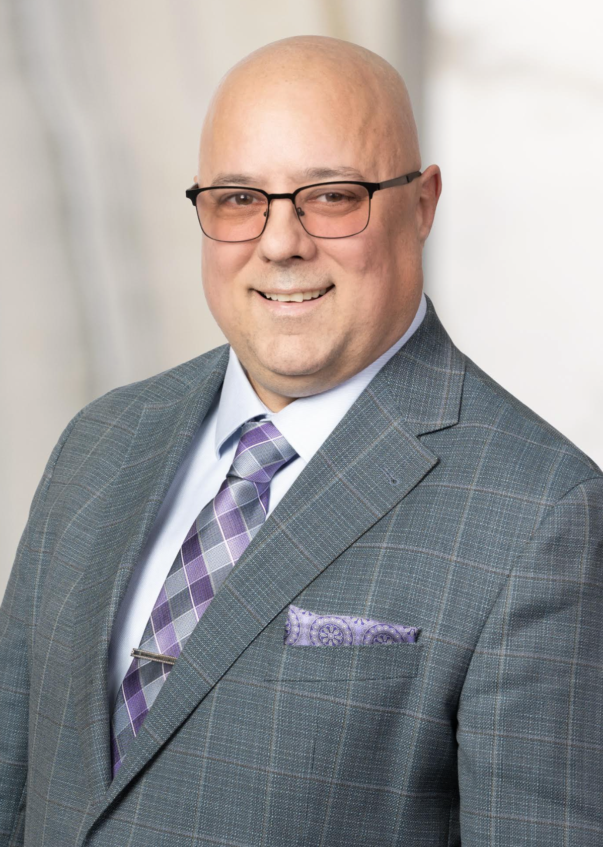 Man wearing gray suit with purple tie, smiling.
