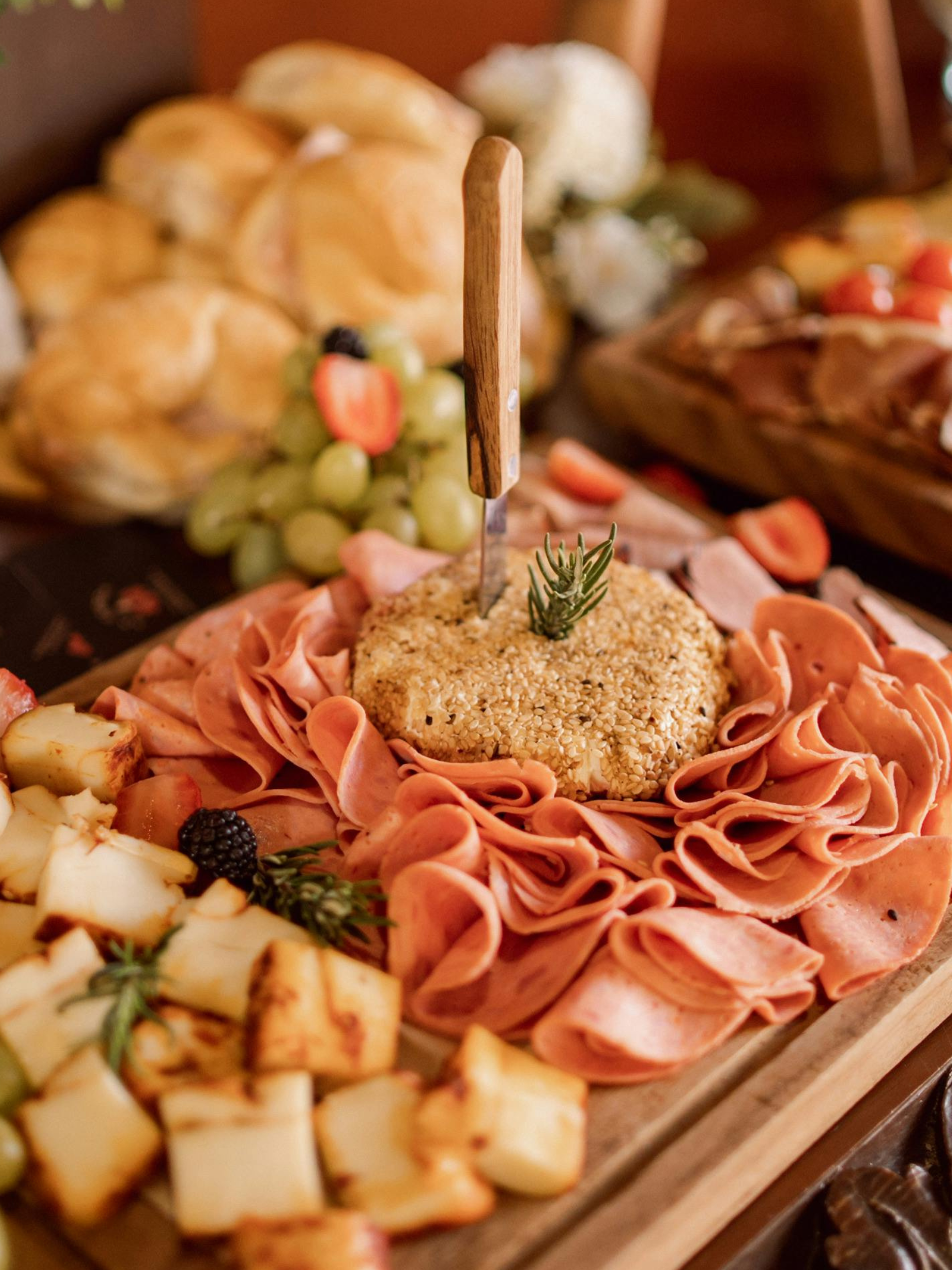 Cheese, sliced meats, grapes, strawberries, blackberries, and bread on a charcuterie board.