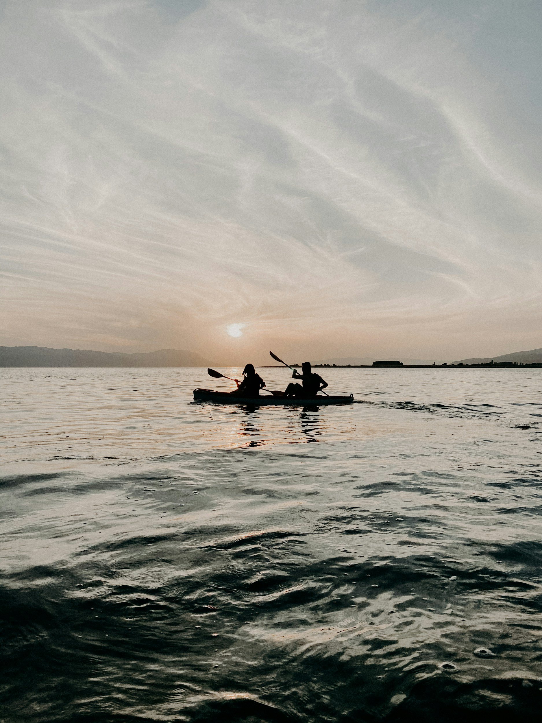 Silhouettes de deux personnes en kayak sur un lac au coucher du soleil avec un ciel nuageux.