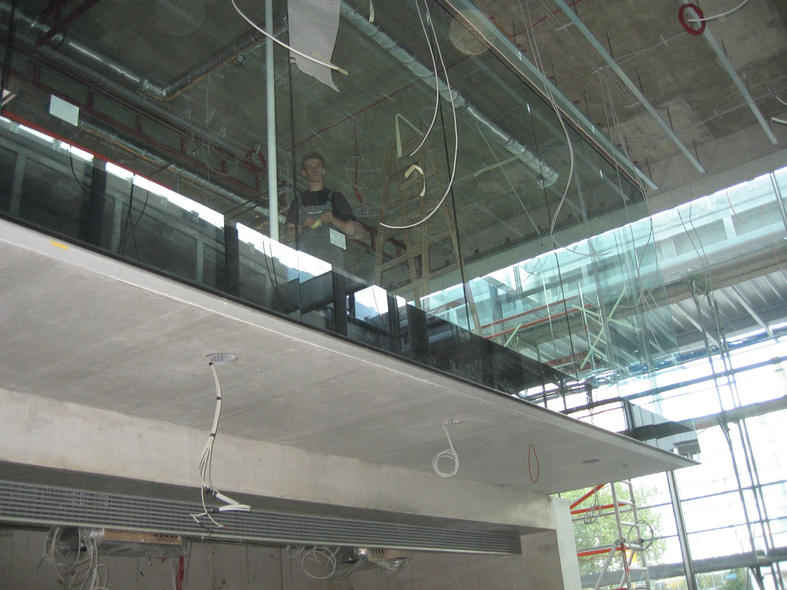 Innenansicht eines Gebäudebaus im Rohbau, mit sichtbarer Decke, scaffolding, Kabeln und einer Person, die auf einer Leiter steht, während der Bau im Gange ist.
