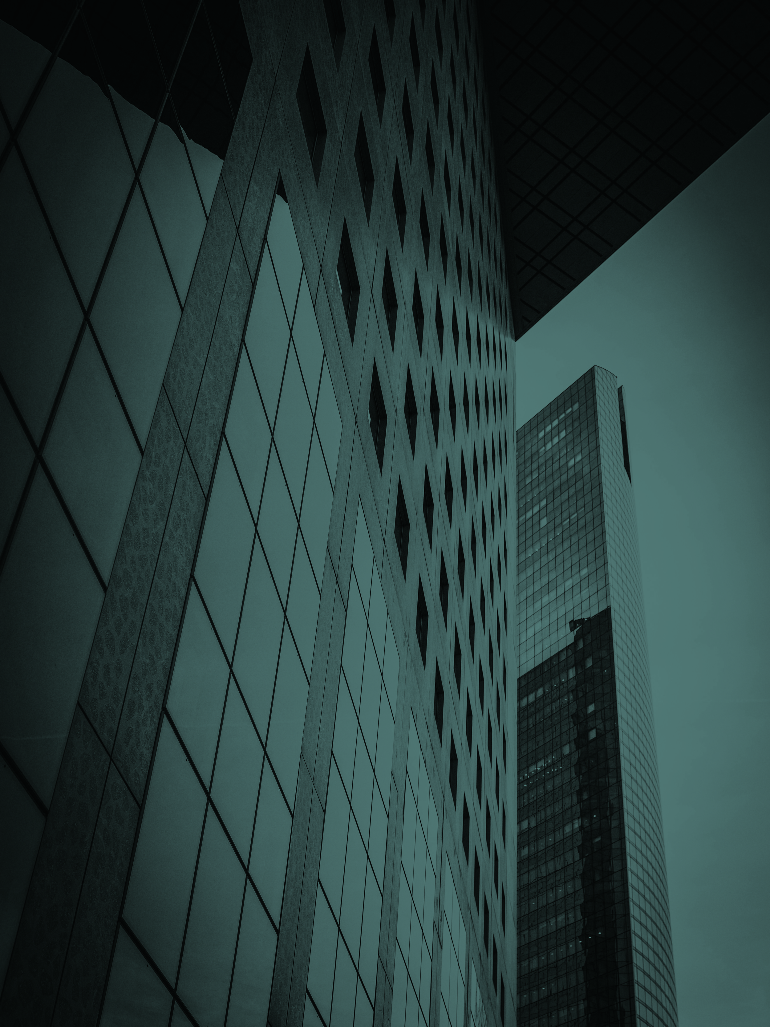 Low-angle view of modern skyscrapers with glass facades in a city skyline, under an overcast sky.