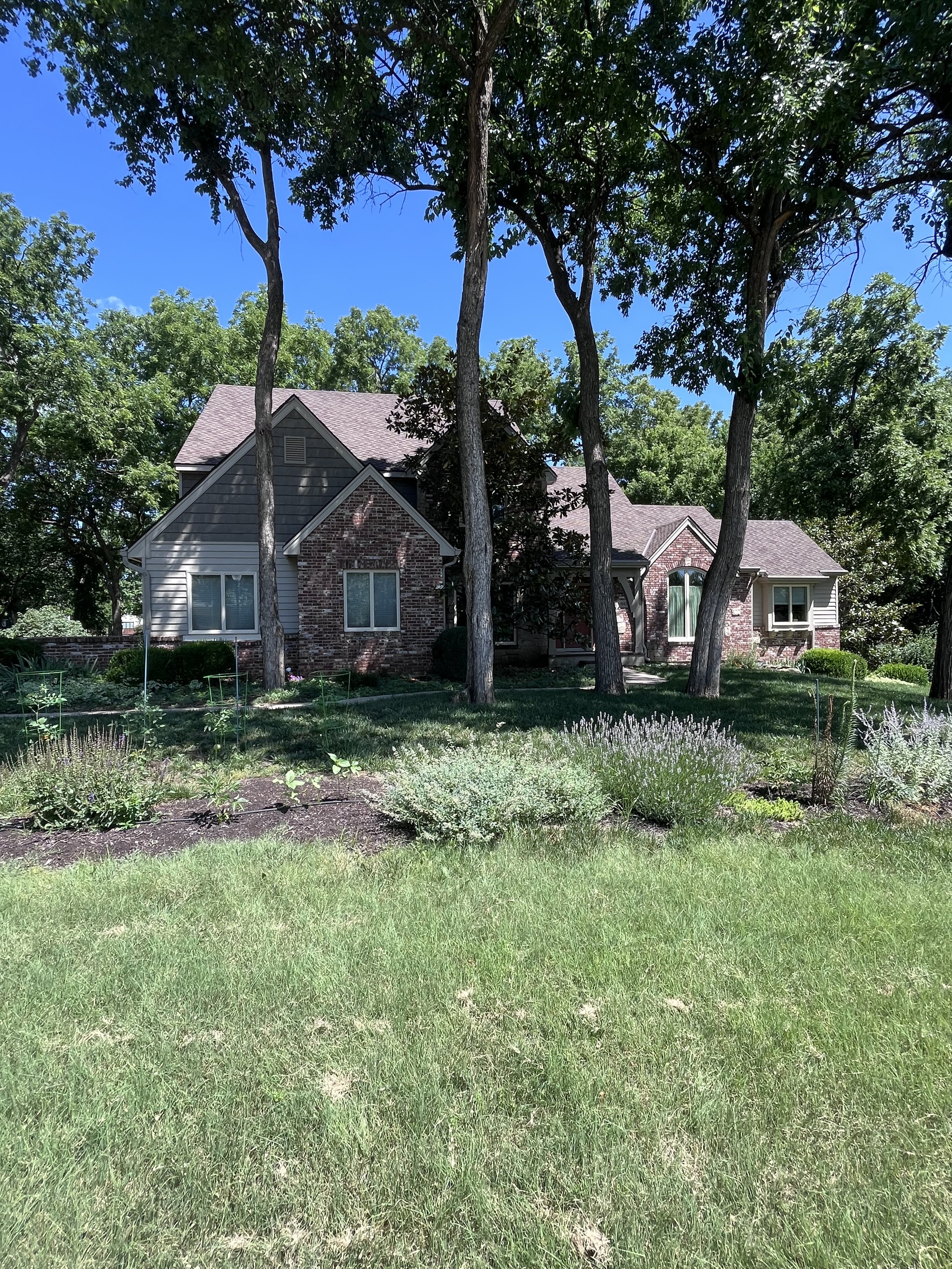 Front view of a brick and siding house surrounded by tall trees and a well-maintained lawn.