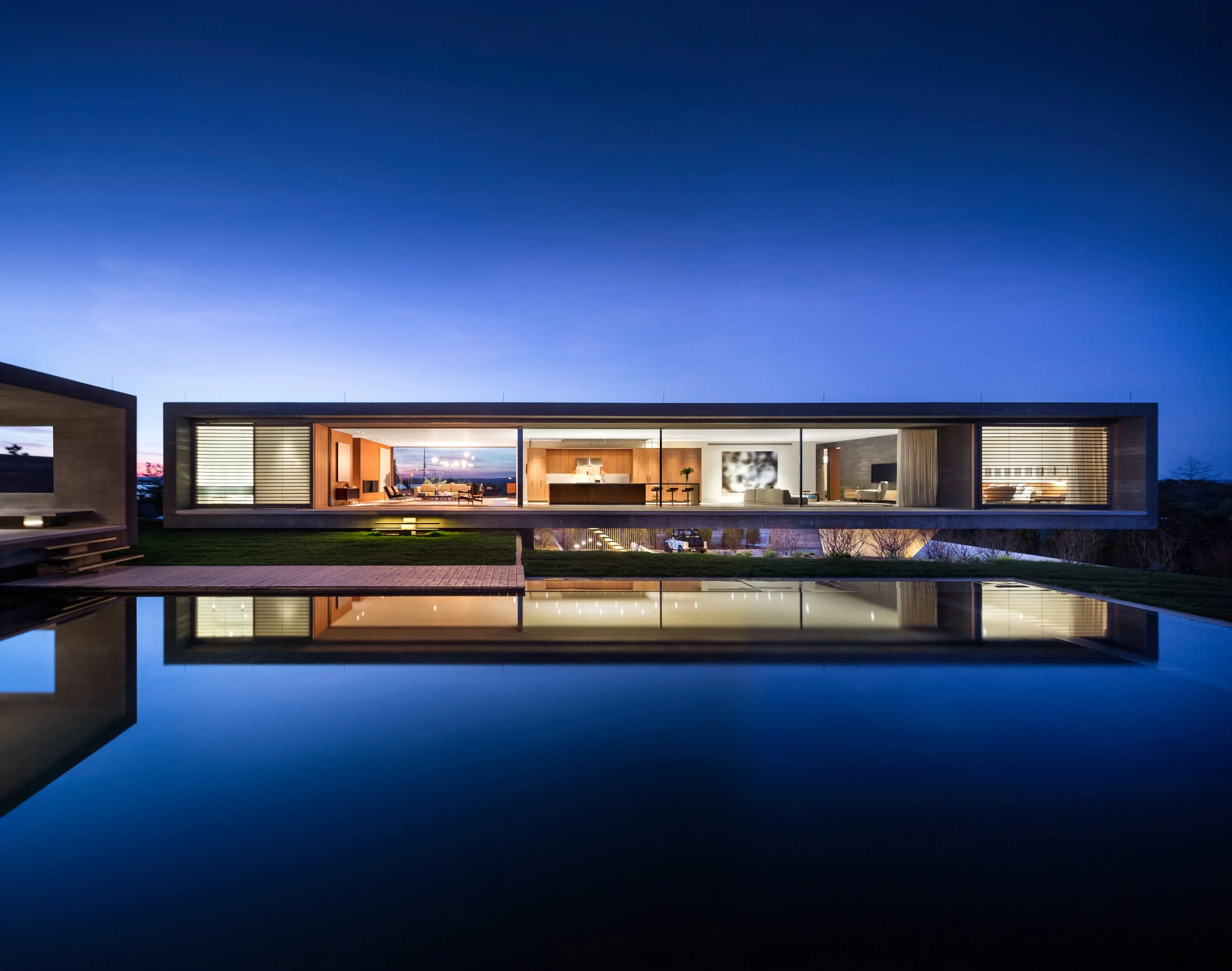 Modern house with large glass windows reflected in a still pool at dusk.