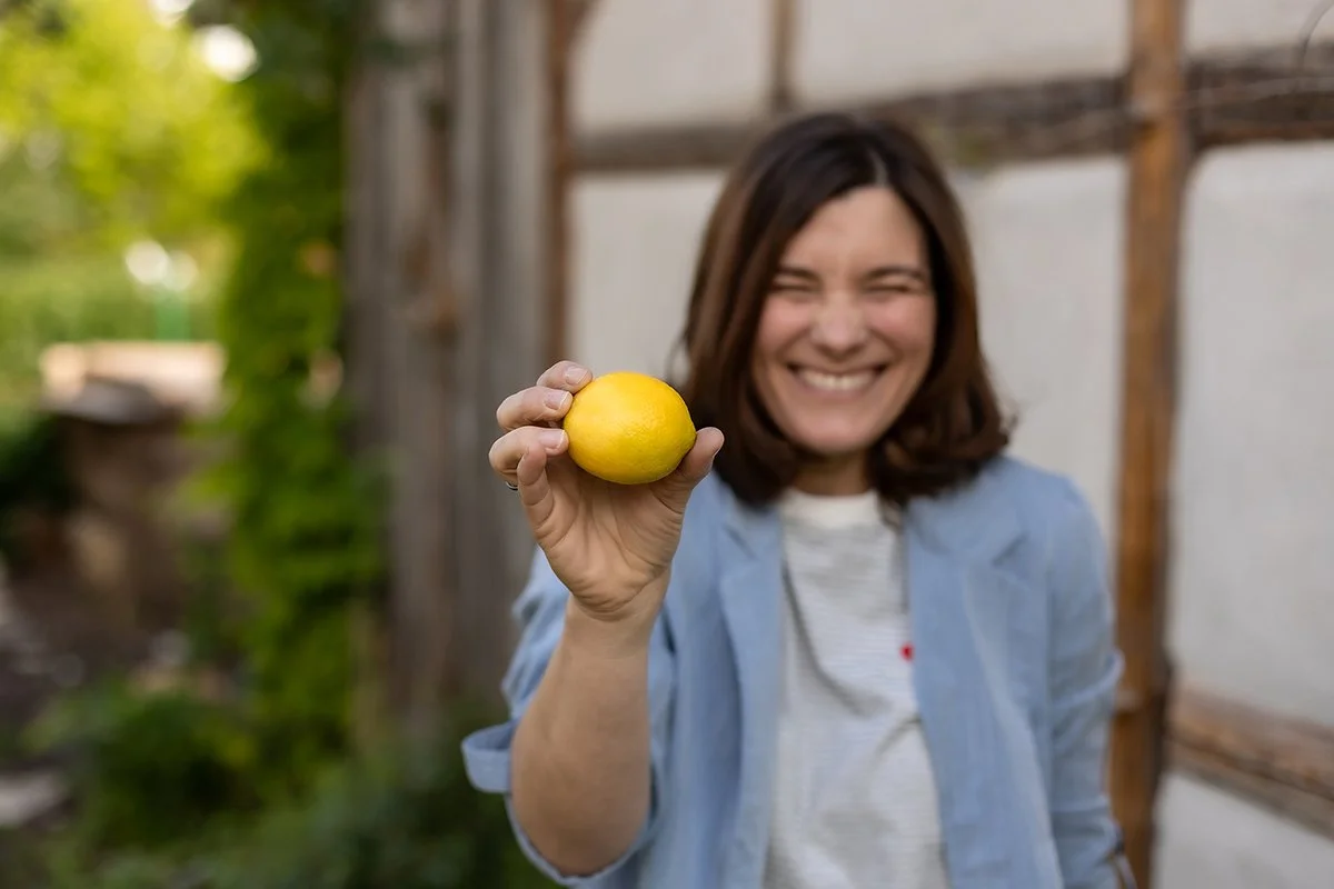 Frau hält eine Zitrone in der Hand, im Garten, lachend.