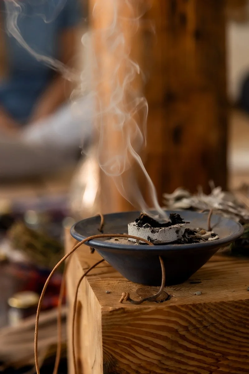 Rauch steigt aus einer mit Kohle erhitzten Räucherschale auf einem Holzblock auf – Teil eines traditionellen Räucherrituals zur Raumklärung.