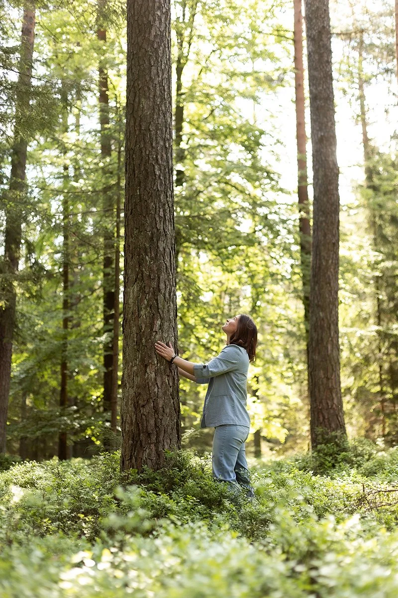 Eine Frau umarmt einen Baum im grünen Wald bei Sonnenlicht.
