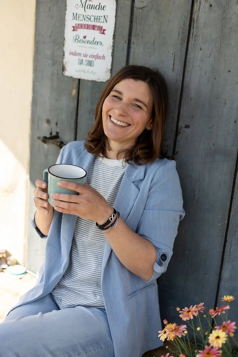 Anja Haselhofer in entspannter Atmosphäre mit Tasse und Blumen – persönliche Ansprechpartnerin für Entspannung, Achtsamkeit und Wohlbefinden.