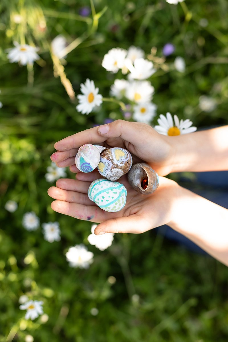 Kind zeigt bunte, selbst gestaltete Schneckenhäuser und verbindet Kreativität mit Naturerlebnis.