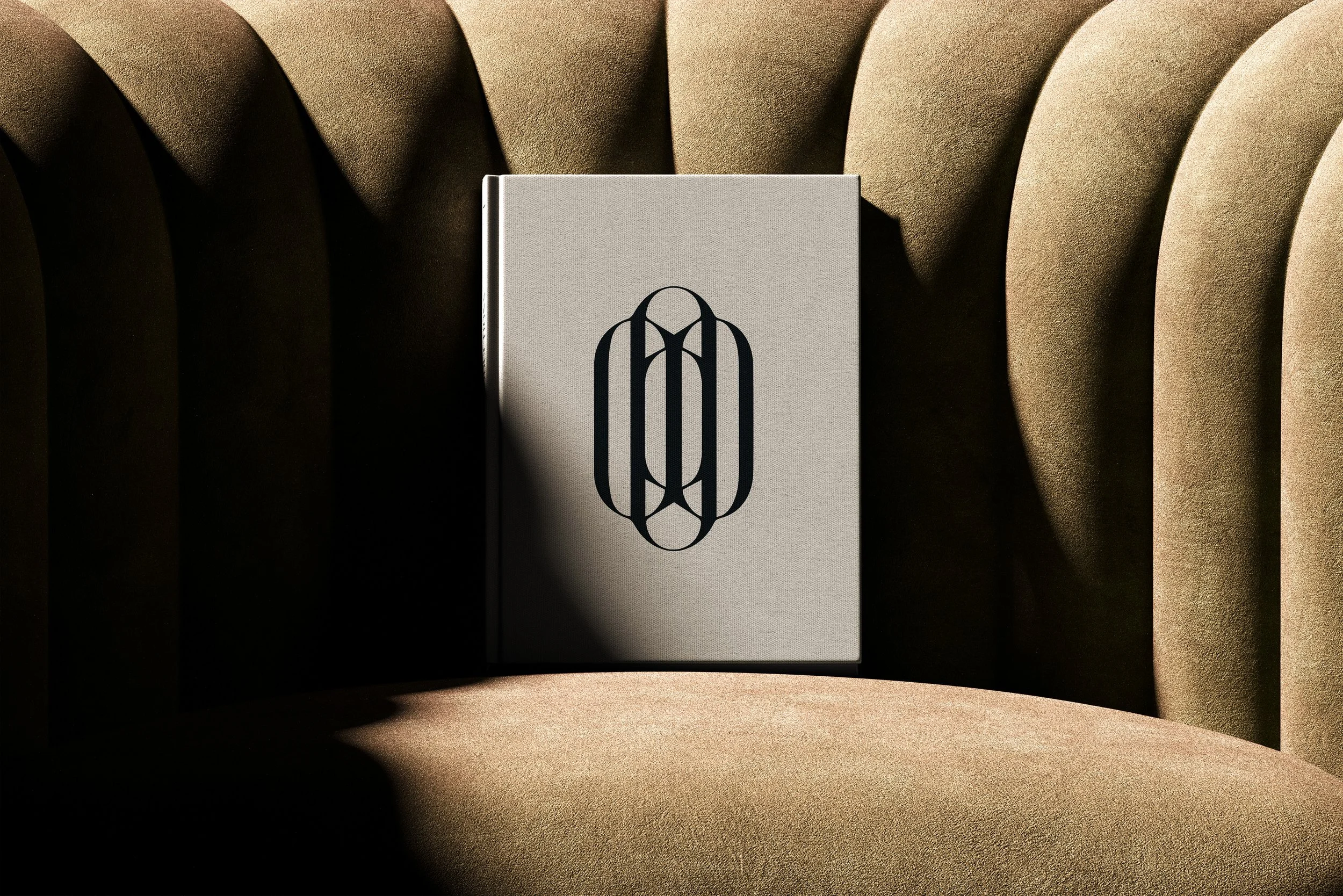 Présentation du book de Wonderland Productions (cabinet d’architecture) avec une couverture beige et le logo noir, posé sur un fauteuil en tissu beige avec des plis.
