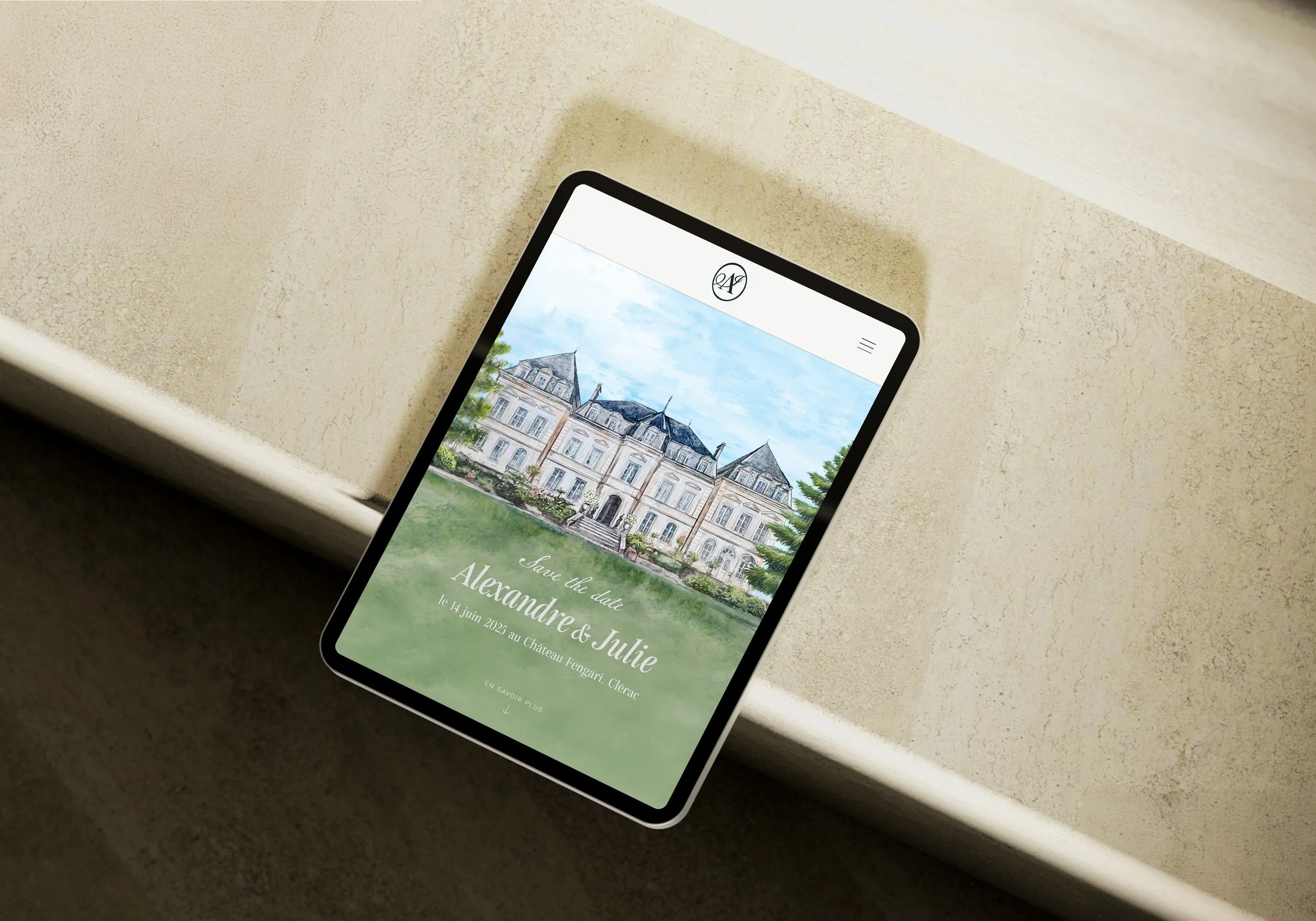 Tablette affichant le site de mariage J&A avec une illustration d'un château en arrière-plan, sur une table beige.