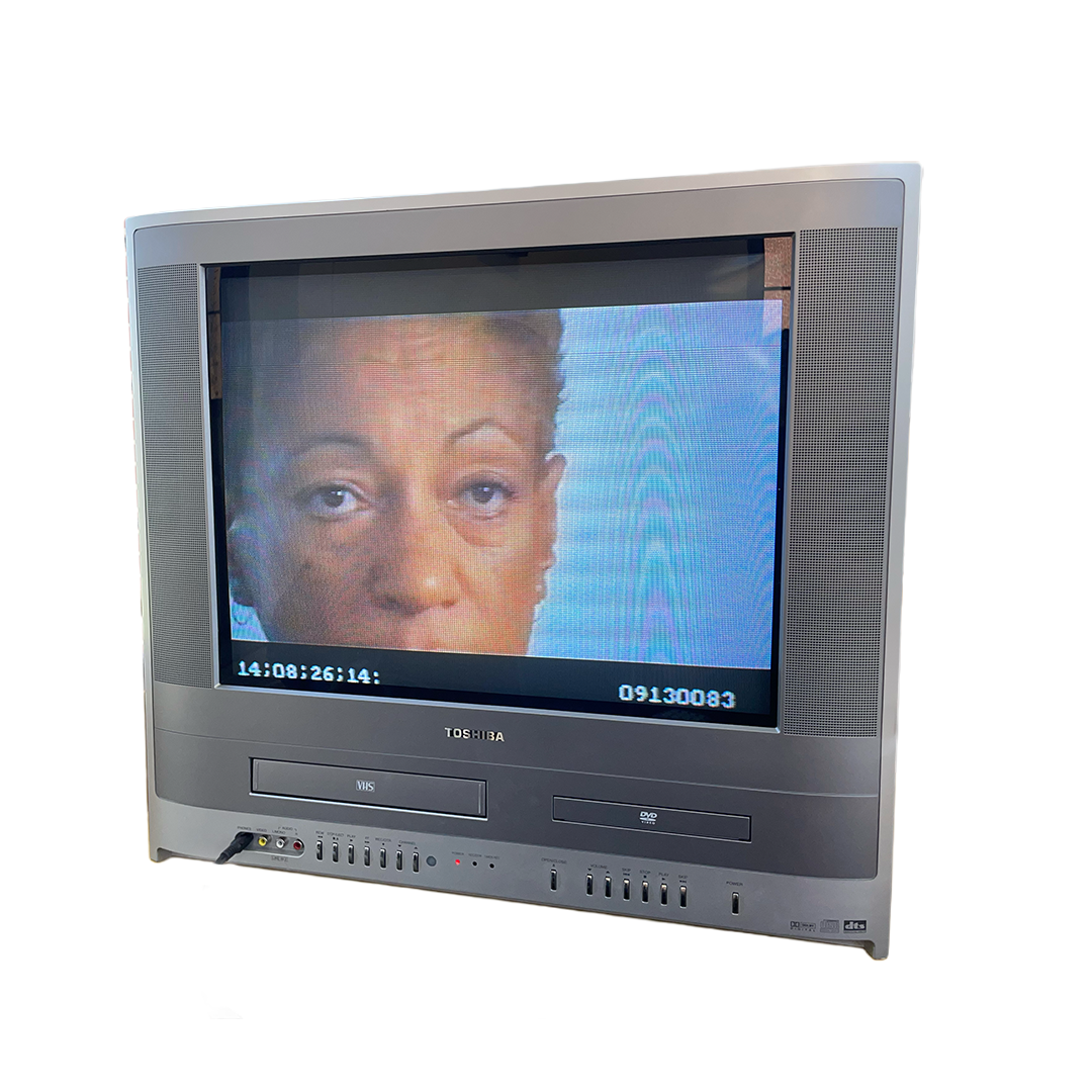 Close-up of a vintage Toshiba CRT television showing a woman's face on the screen, placed on a yellow table in a room.