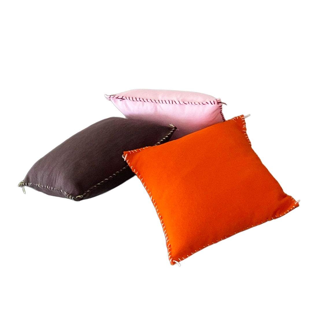 Three colorful throw pillows—pink, black, and orange—stacked on top of each other.