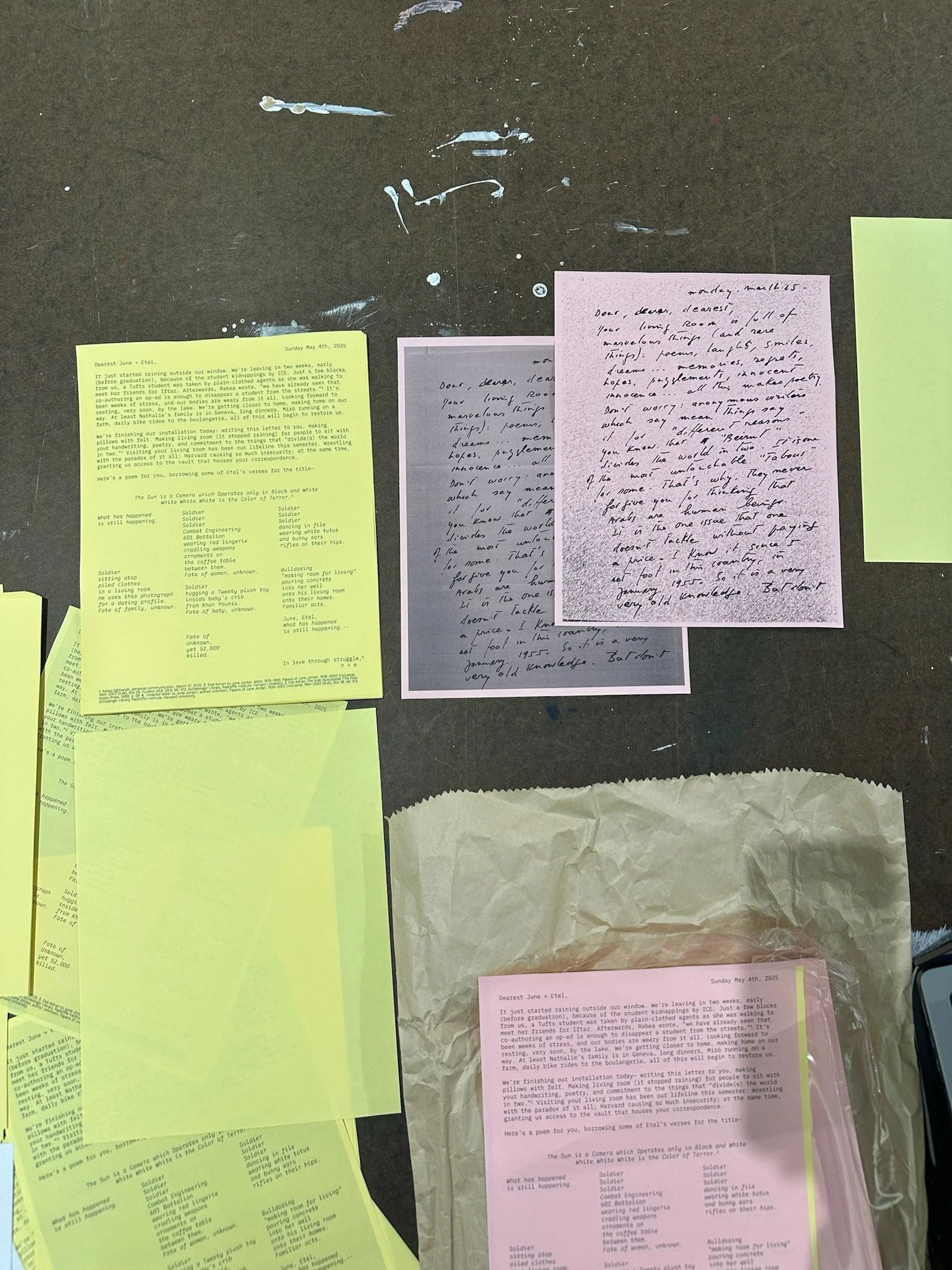 Various handwritten and printed papers on a dark surface, including a yellow sheet, a pink sheet, and a gray sheet, some with handwritten notes and others with printed text.