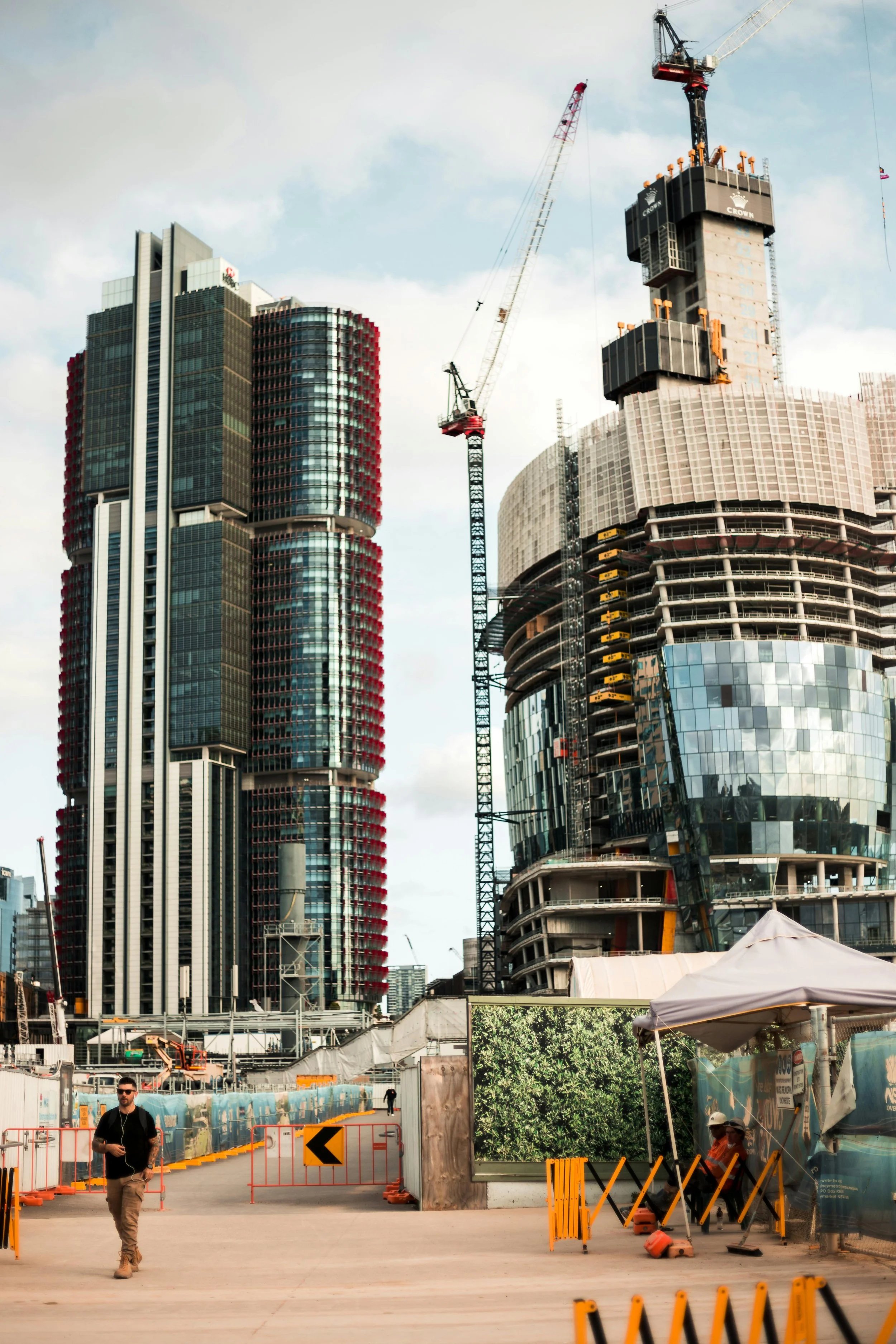 Cityscape with high-rise buildings under construction, cranes, construction barriers, and people walking.